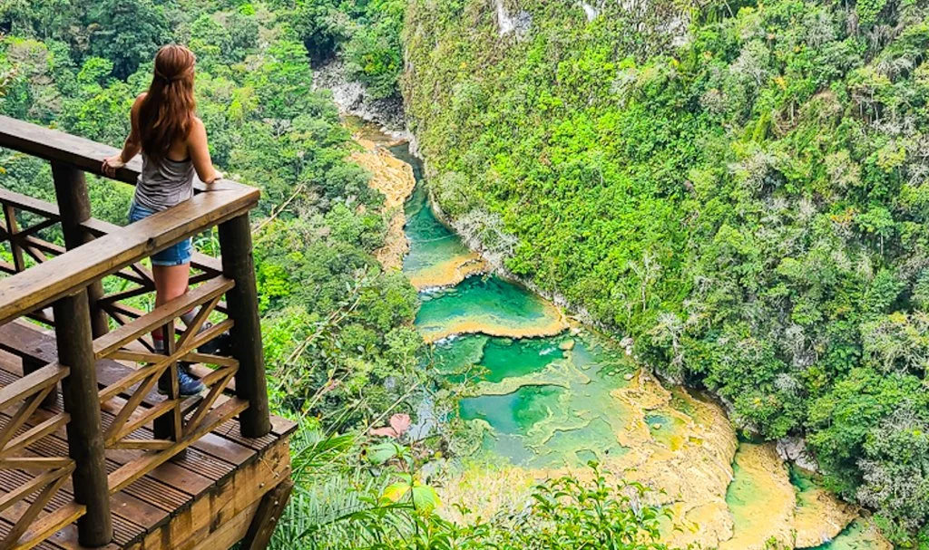 woman standing on a deck overlooking the jungle and a series of green waterfalls