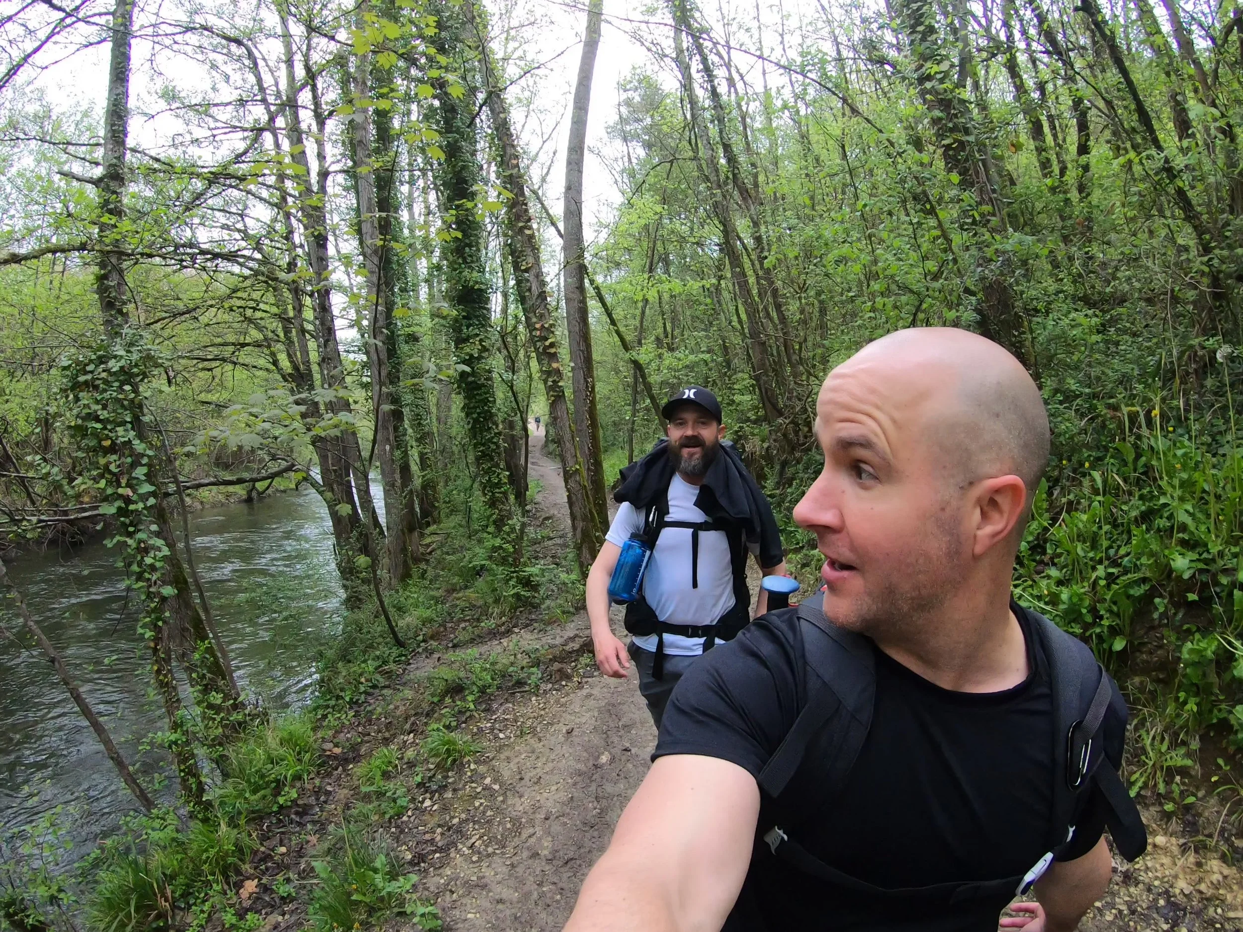 Man walking with friends on a wooded trail filming himself