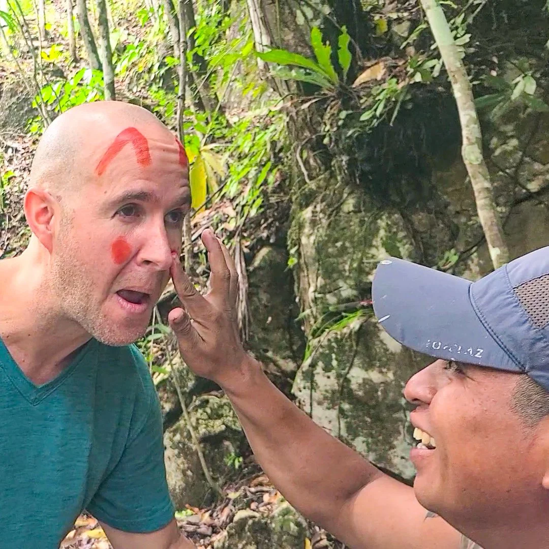 Two men in a jungle, one with red face paint, the other wearing a blue cap, appear to be having a conversation or confrontation.