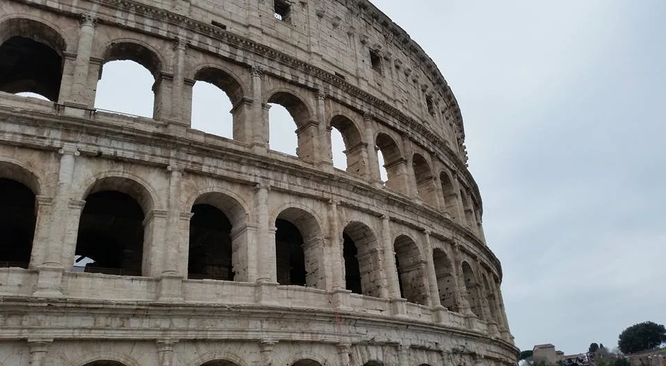 Close-up of the Roman Colosseum's stone arches and exterior structure under a cloudy sky.