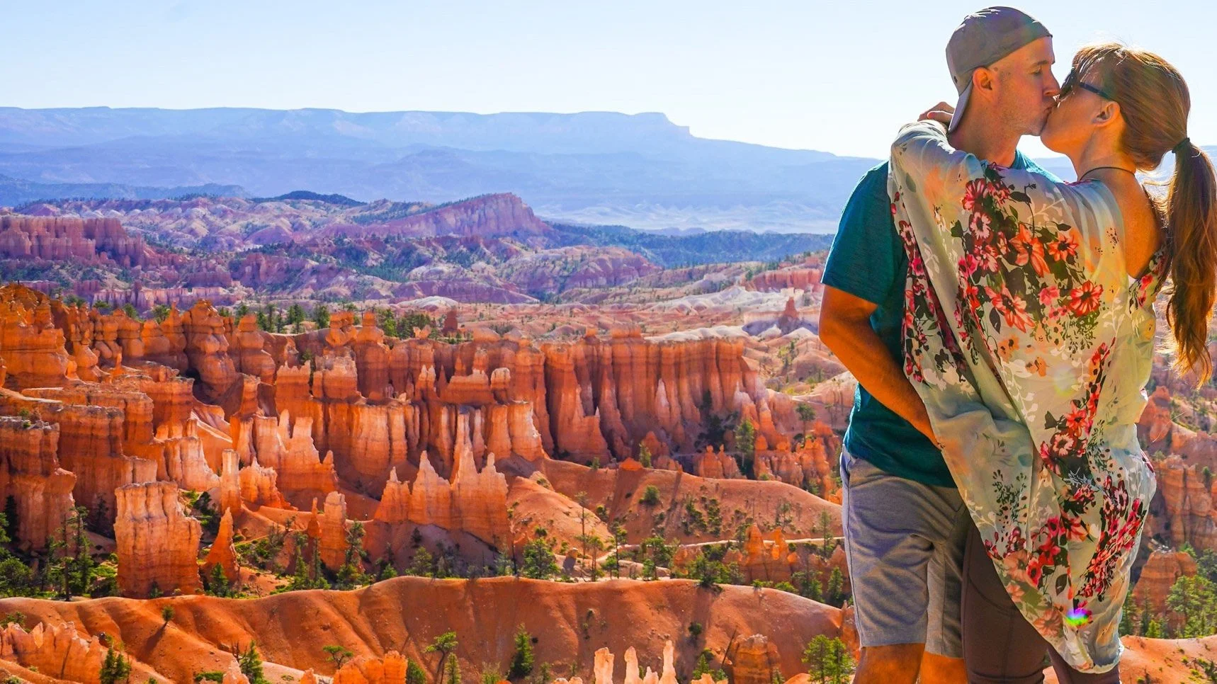 A couple sharing a kiss at Bryce Canyon with colorful hoodoos and a clear blue sky in the background.