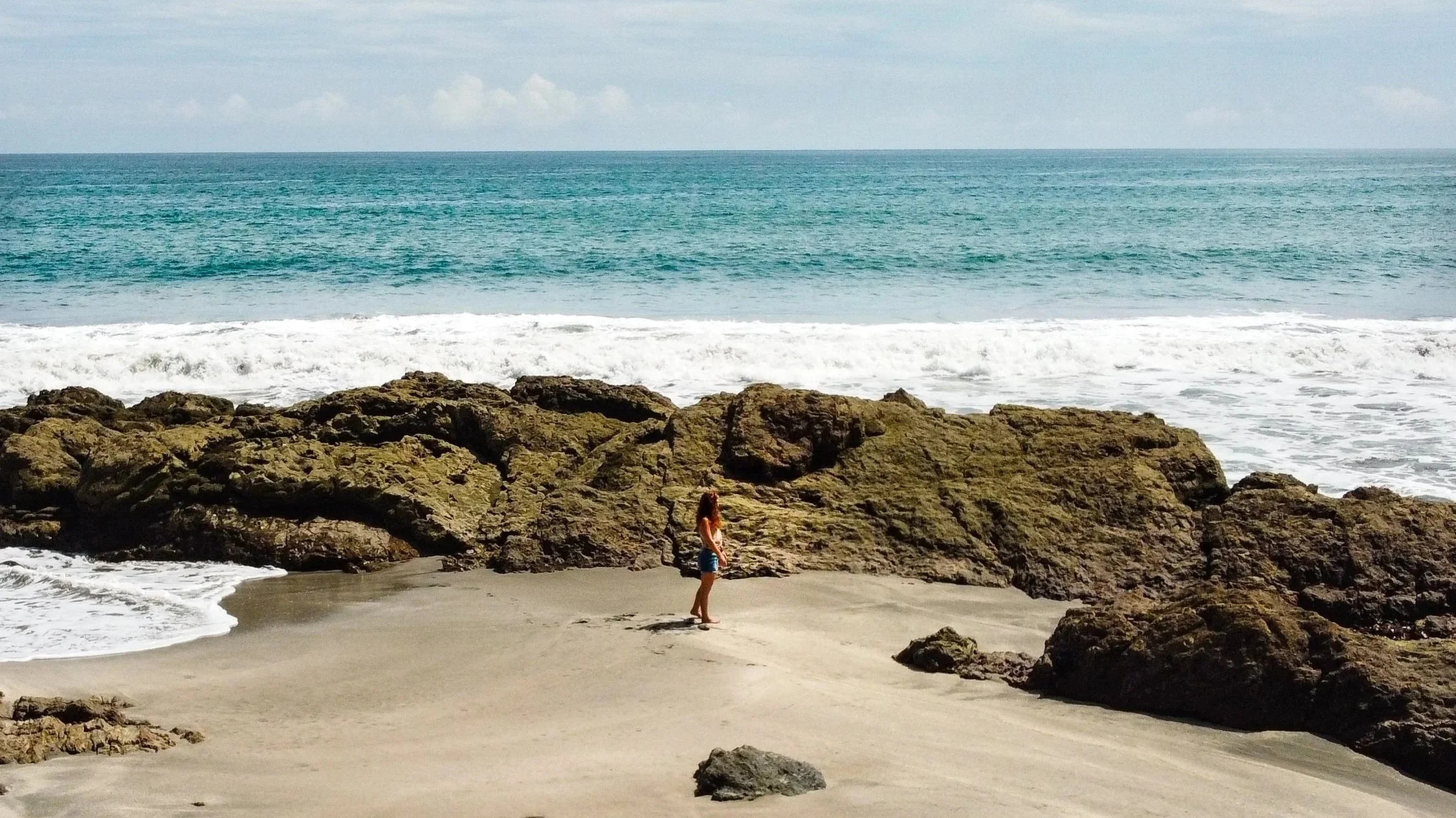woman walking on gold beach with rocks and wild waves in the background