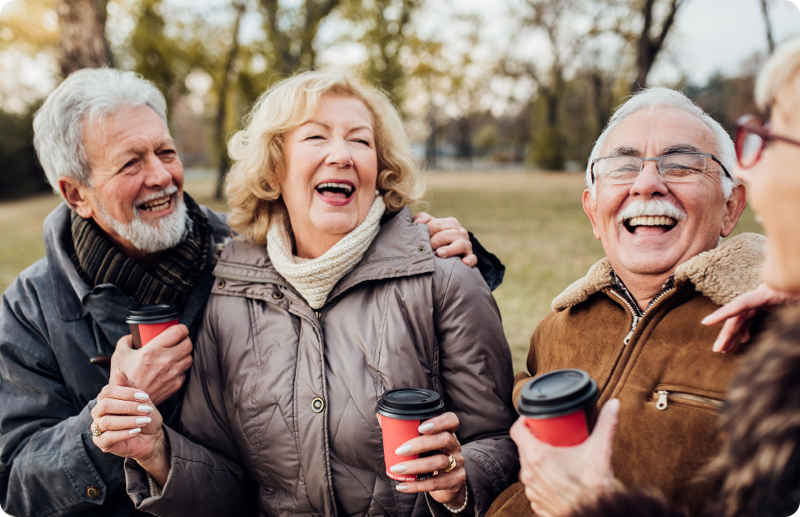 Older friends laughing together outdoors with coffee