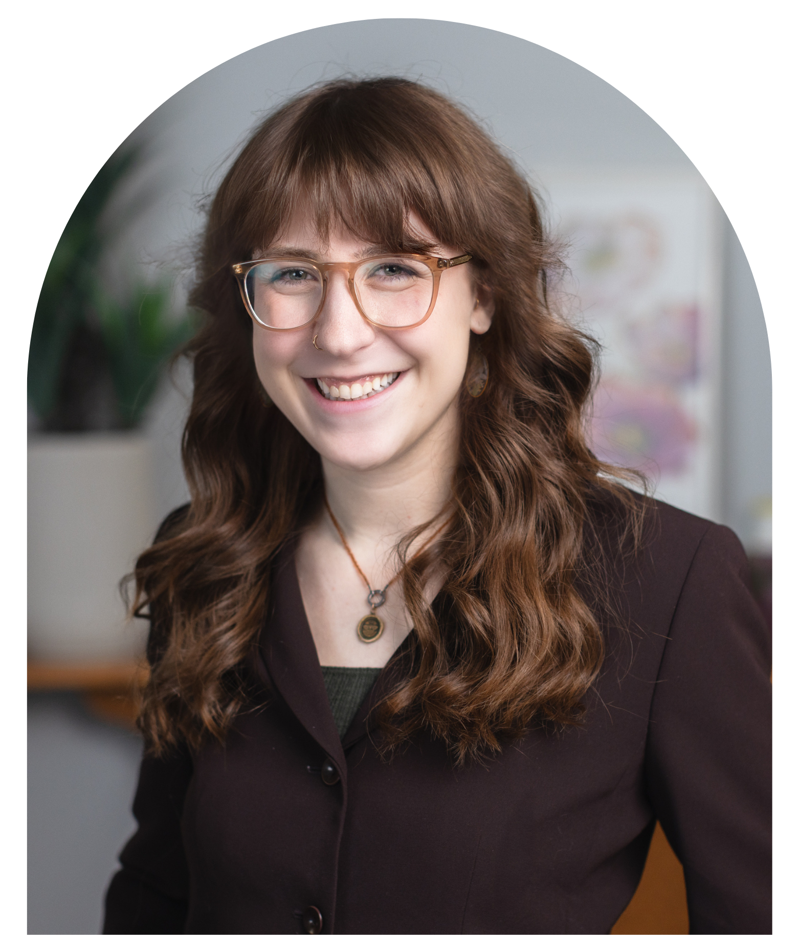 Portrait of Jocelyn Podolsky, health promotion advisor. She has long wavy brown hair, glasses, and a nose ring smiling in an indoor setting.