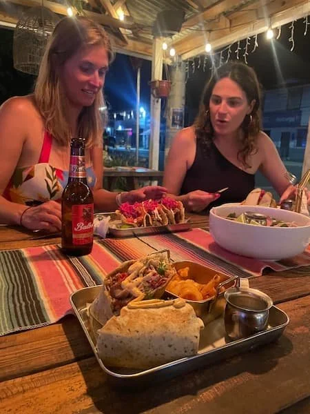 Two women enjoying burritos, tacos, and cold Balboa beer during a community dinner at The Experience Surf Camp.