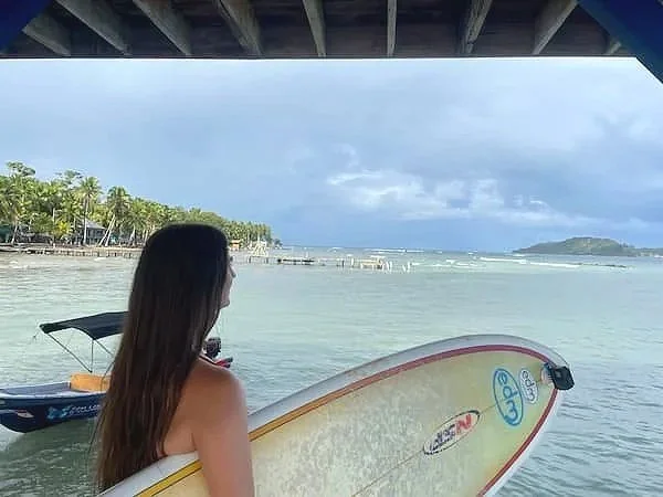 A female surf student from The Experience Surf Camp holding her surfboard and looking out at the ocean in Bocas del Toro, Panama.