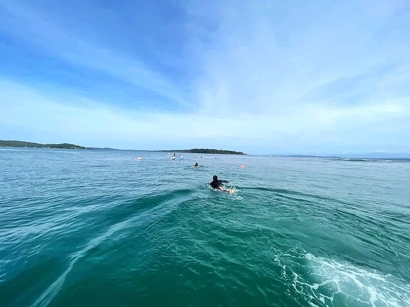 Surfers from The Experience Surf Camp paddling out in the clear turquoise ocean during a daily surf session in Panama.