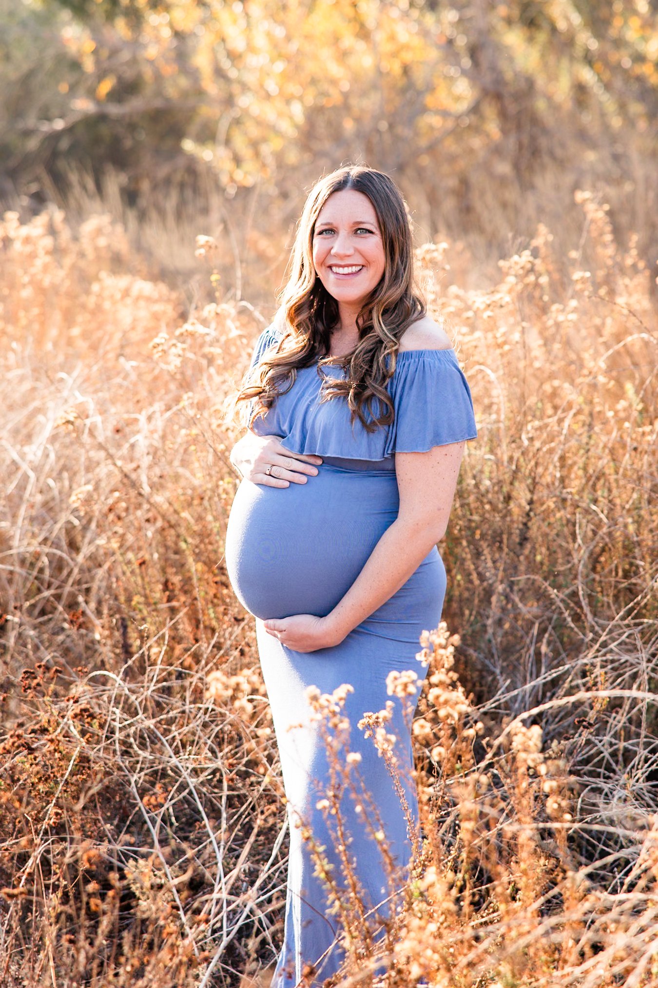 Pregnant woman blue dress smiling grassy field