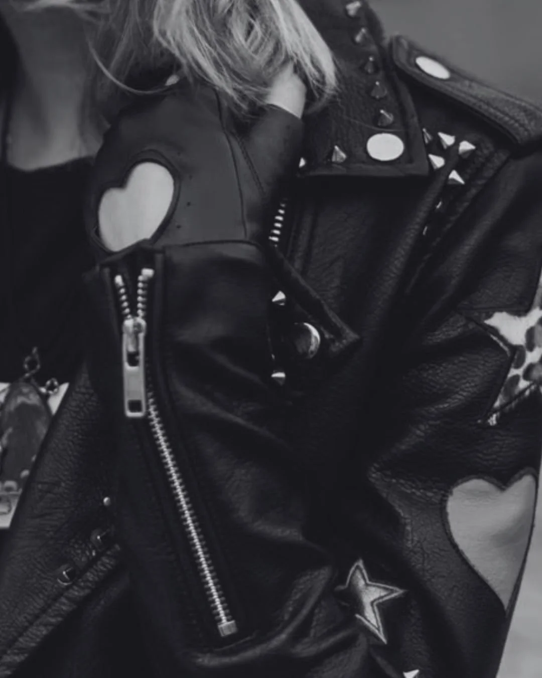 A close up of a black leather jacket decorated with patches and studs.