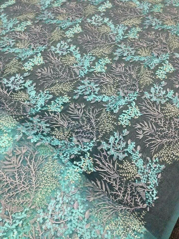 Intricate floral lace fabric with teal and beige embroidery on a dark background.