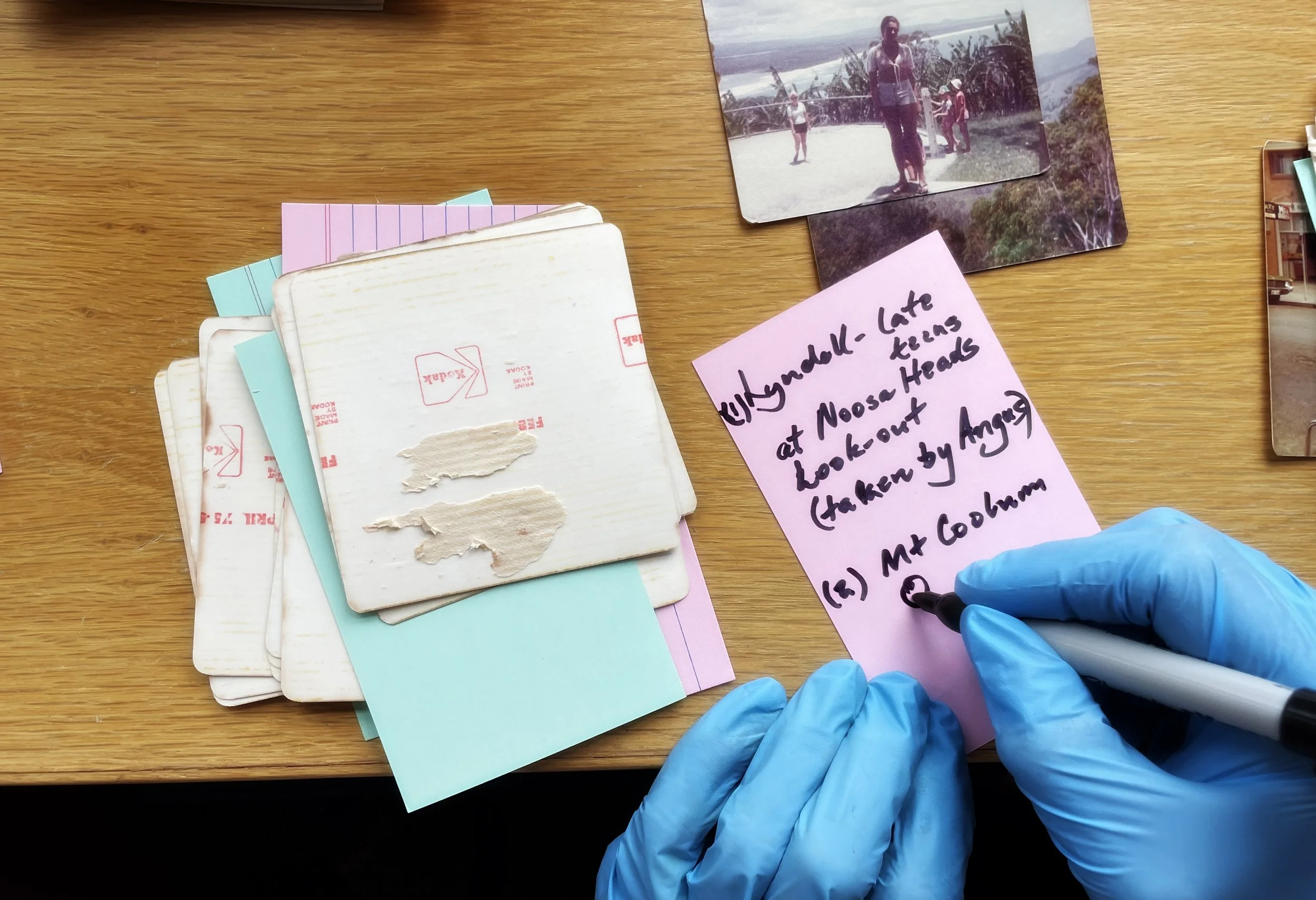 A gloved hand carefully documenting details while sorting printed photographs from the 1970s