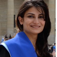 Mona Nasseri smiles in her headshot. She has a piece of blue fabric over her shoulder. In the background is some kind of pillar.