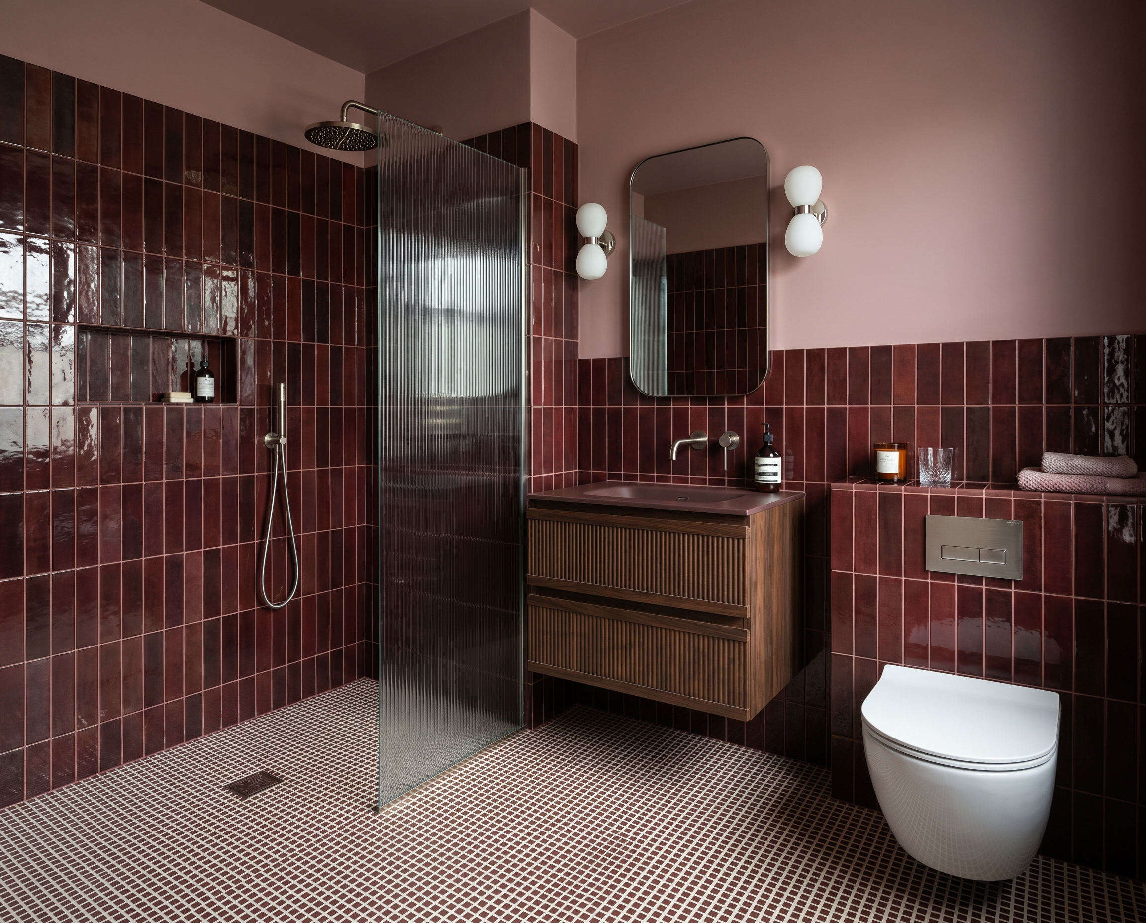 Modern bathroom with red tile walls, a walk-in shower with a metal divider, a wooden vanity with a sink, wall-mounted lights, a mirror, a toilet, and various toiletries and towels.