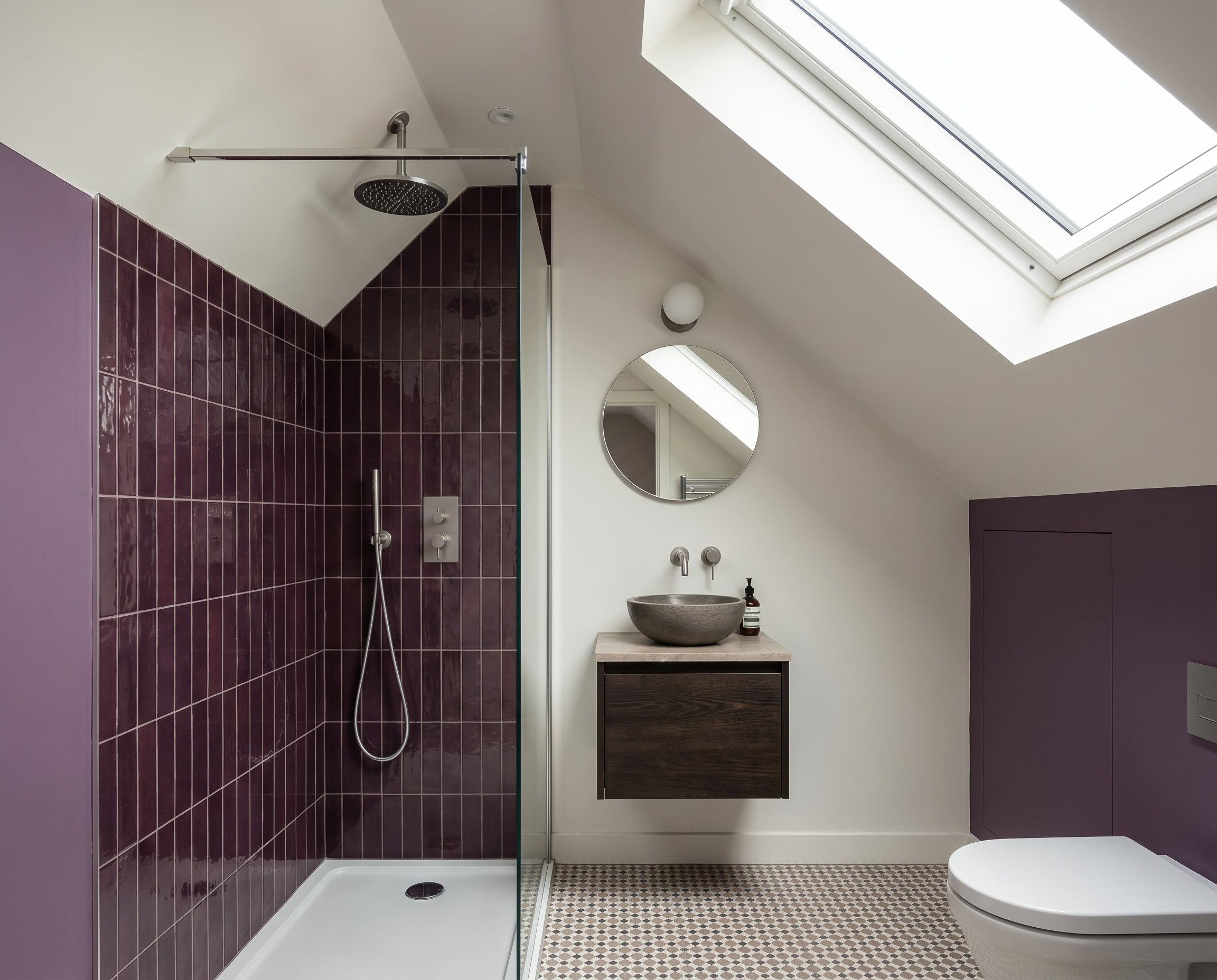 Modern bathroom with purple tiled shower area, round mirror, vessel sink, and skylight.