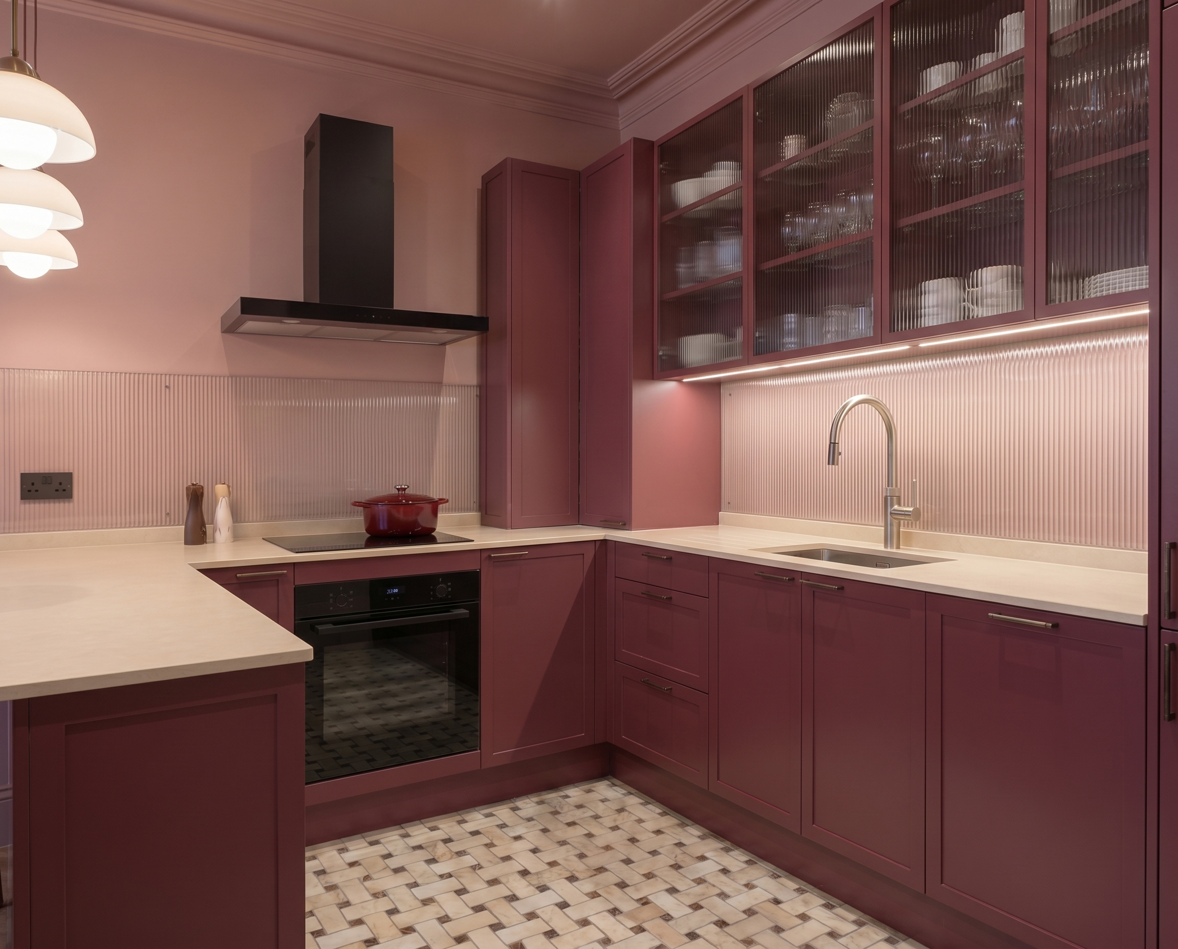 A kitchen with deep purple cabinets, a white countertop, a black stove, and a mosaic tile floor. The upper cabinets have glass doors with shelves of dishes inside. There is a double sink with a modern faucet and under-cabinet lighting.