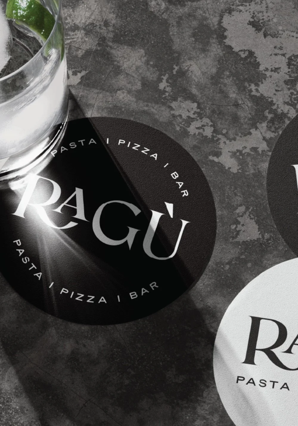 Ragù Pasta Pizza Bar coaster mockup featuring black and white branded coasters on a textured restaurant table surface.