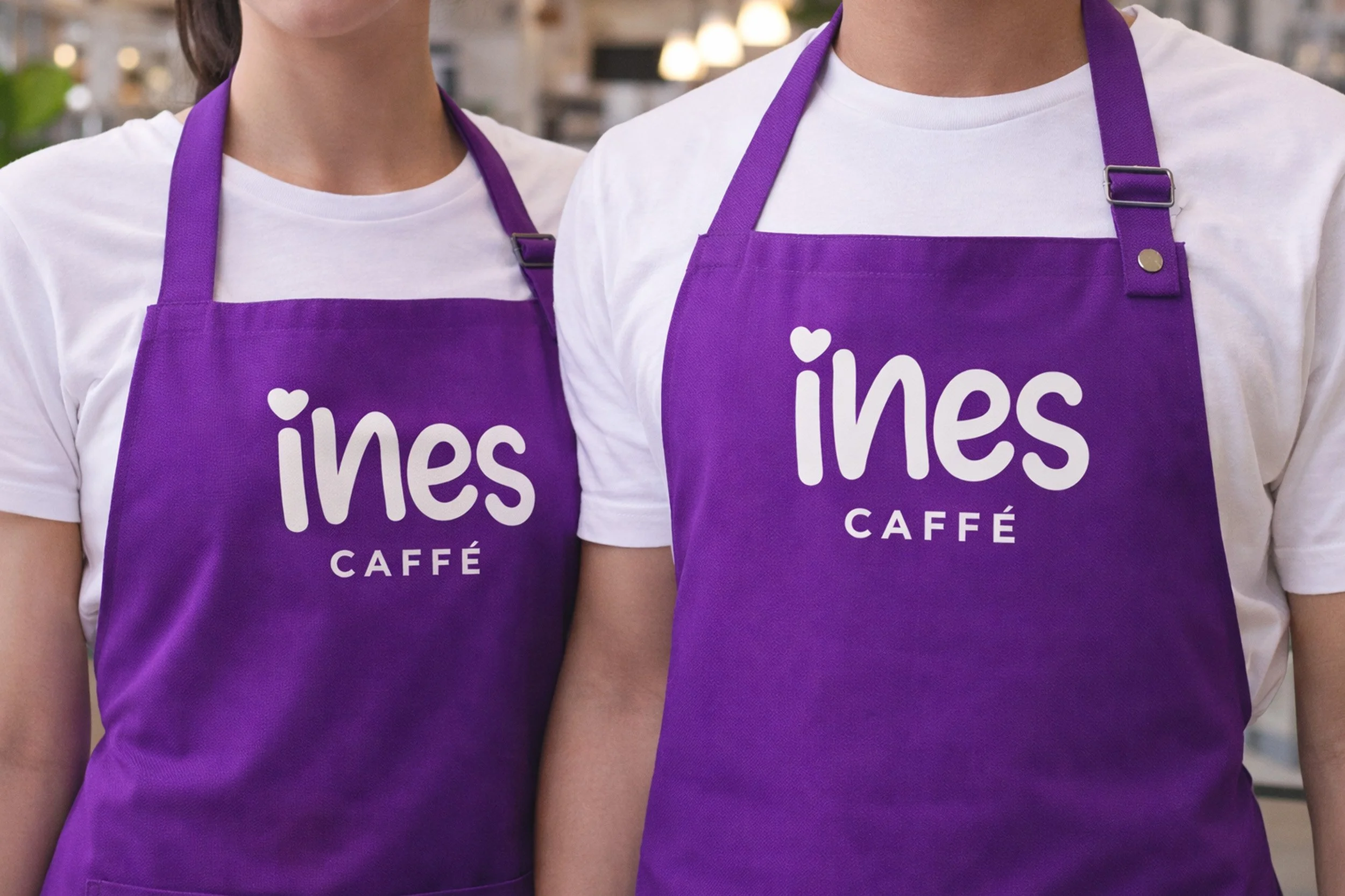 Ines Caffe staff apron uniform mockup featuring purple branded aprons with white logo worn by café staff.