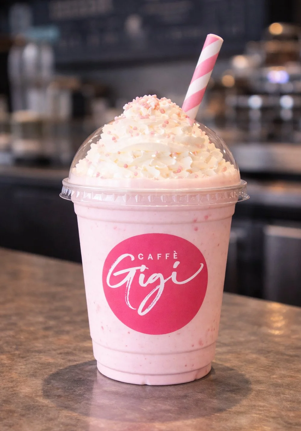 Caffè Gigi pink frappe drink mockup featuring a branded takeaway cup with whipped cream, sprinkles and pink straw in a café setting.