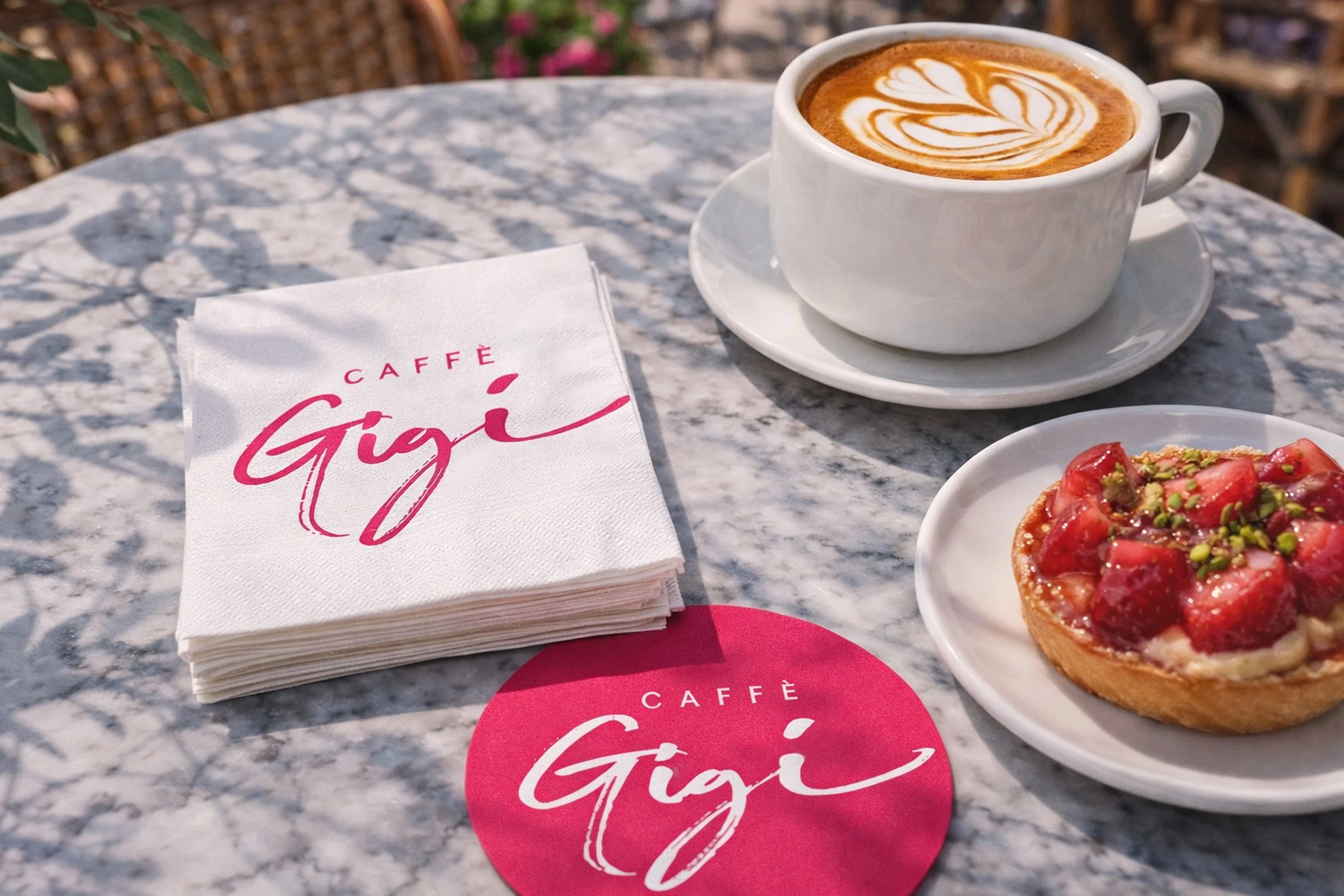 Caffè Gigi café table collateral mockup featuring branded napkins, coaster, cappuccino and strawberry tart on a marble café table.