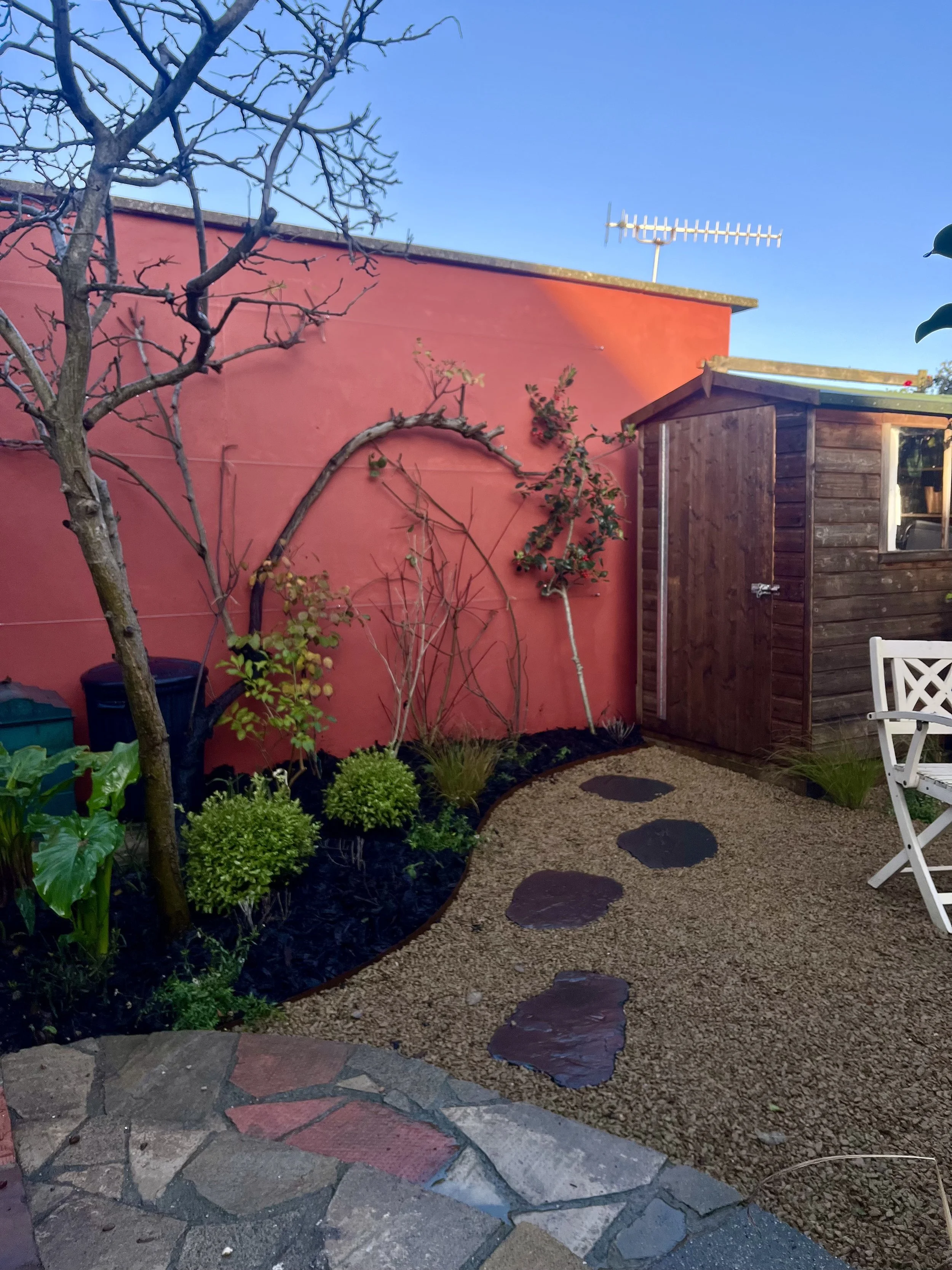 Red painted wall in the Green Boys garden in Saltdean, Brighton & Hove, Sussex. Japanese Slate stepping stones in shingle