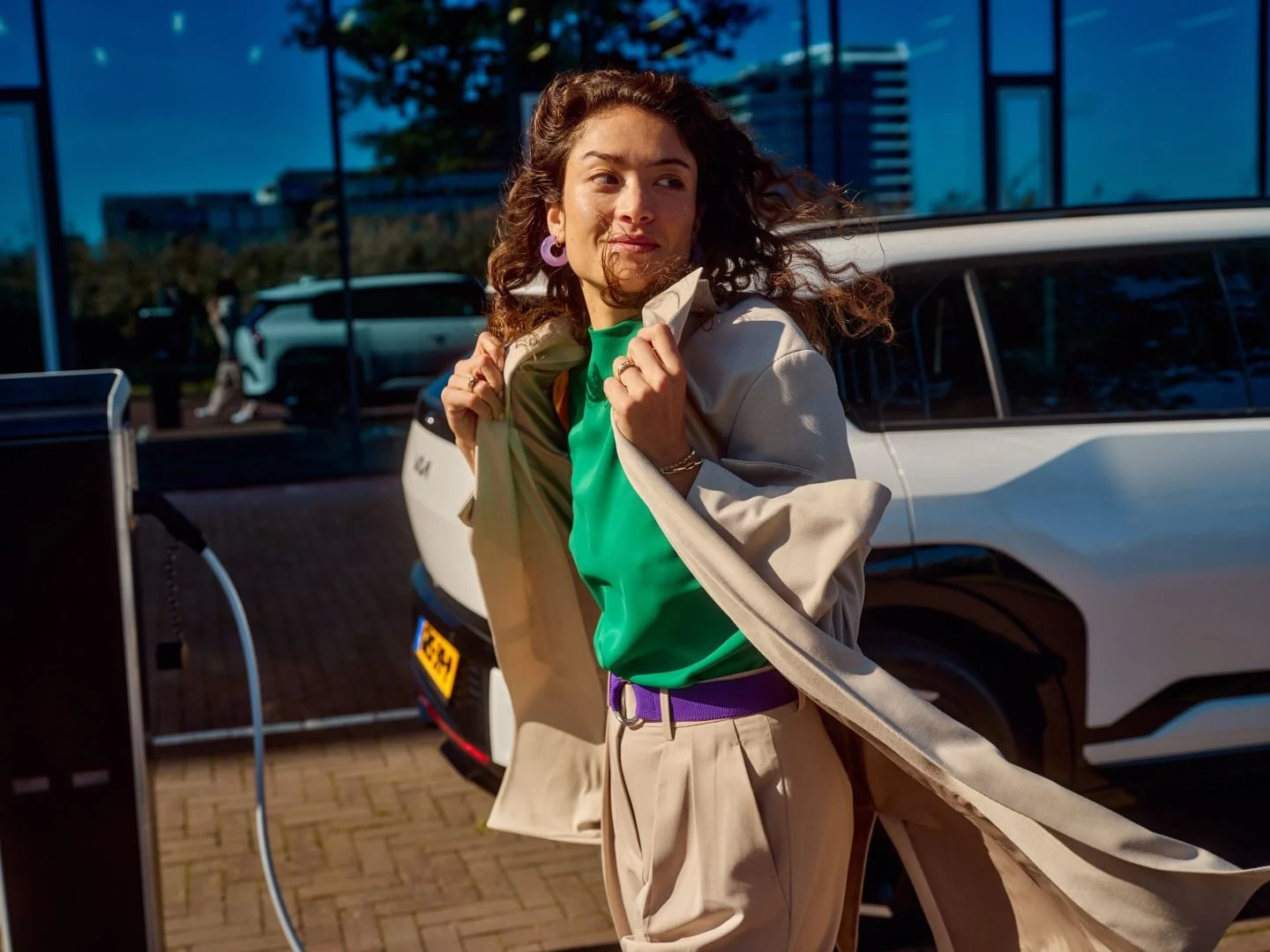 Woman in a coat blowing in the wind at a charging station, Athlon Car Lease shoot in Amsterdam