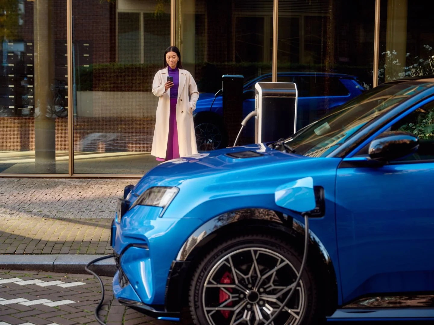 Woman checking her phone at a public charging station, Athlon Car Lease shoot in Amsterdam