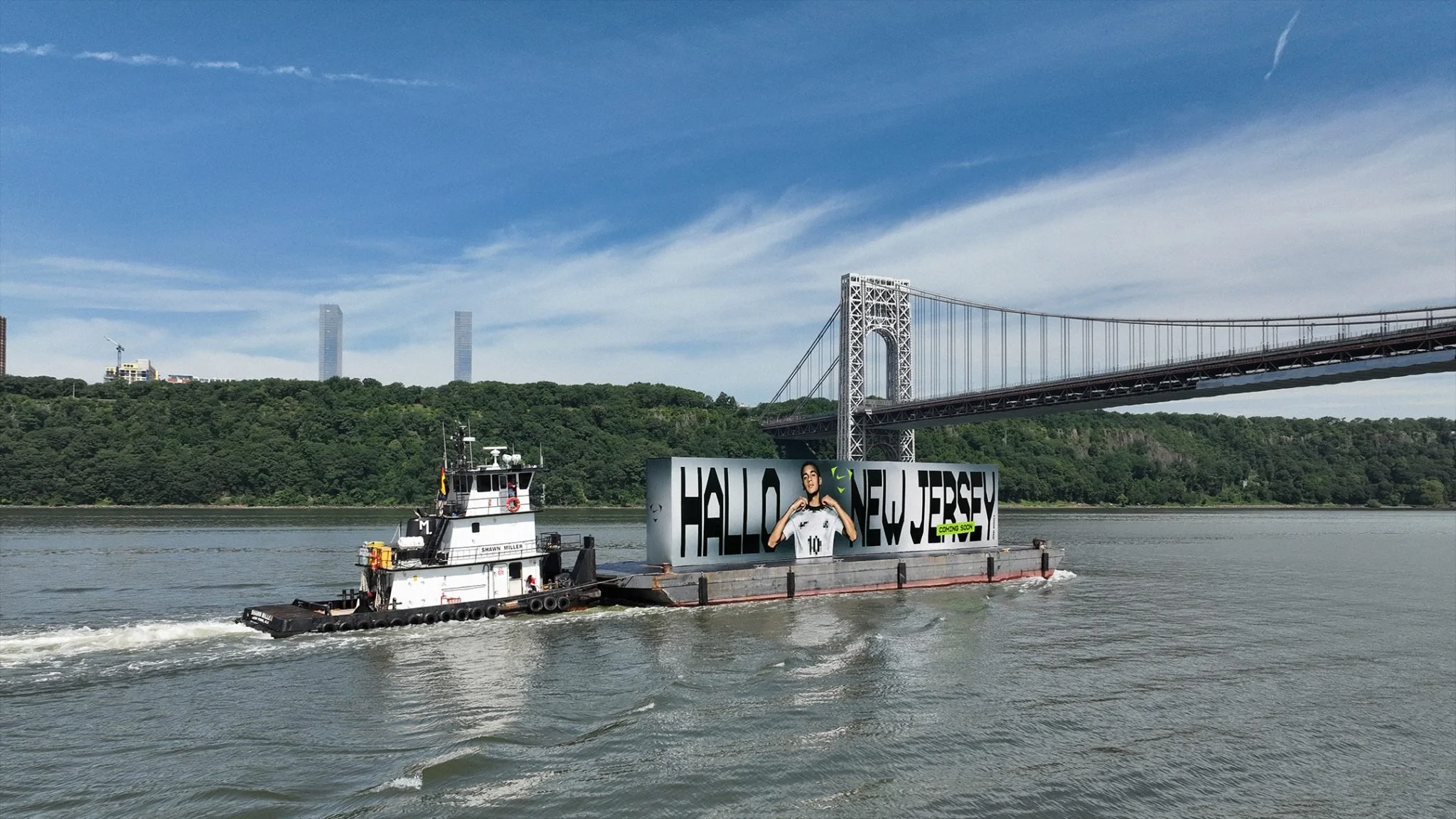 Tugboat pushing the 'Hallo New Jersey' billboard barge past the George Washington Bridge, Nike Football Jamal Musiala World Cup 2026