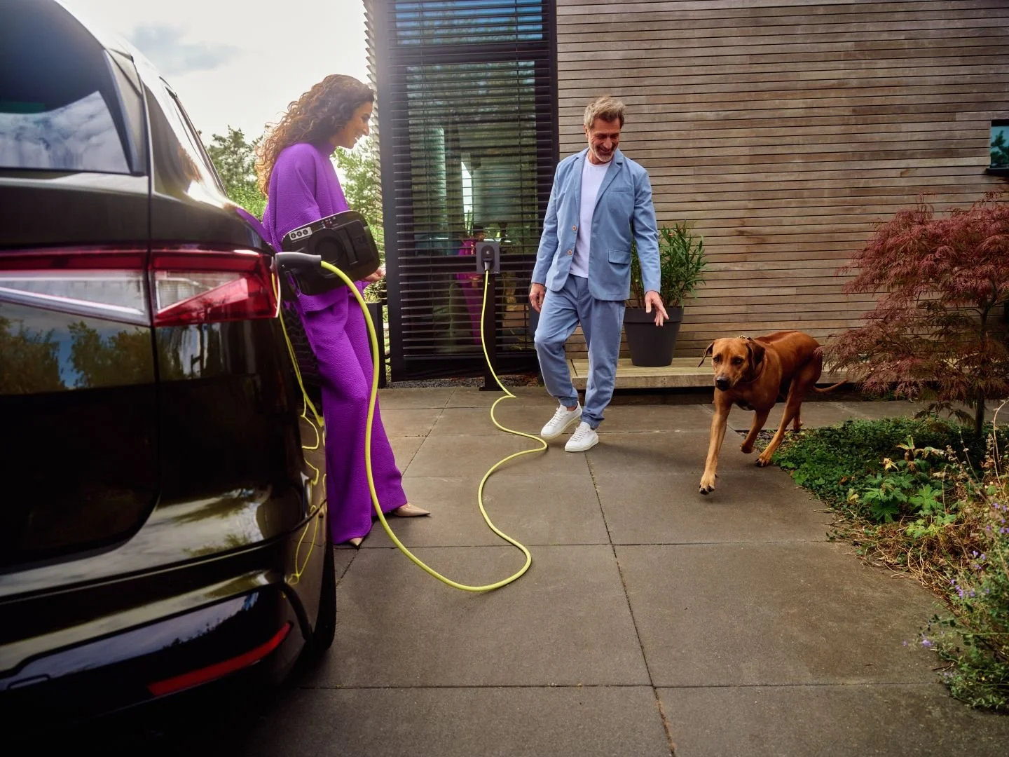 Couple with their dog next to an electric car charging at home, Athlon Car Lease shoot in Amsterdam