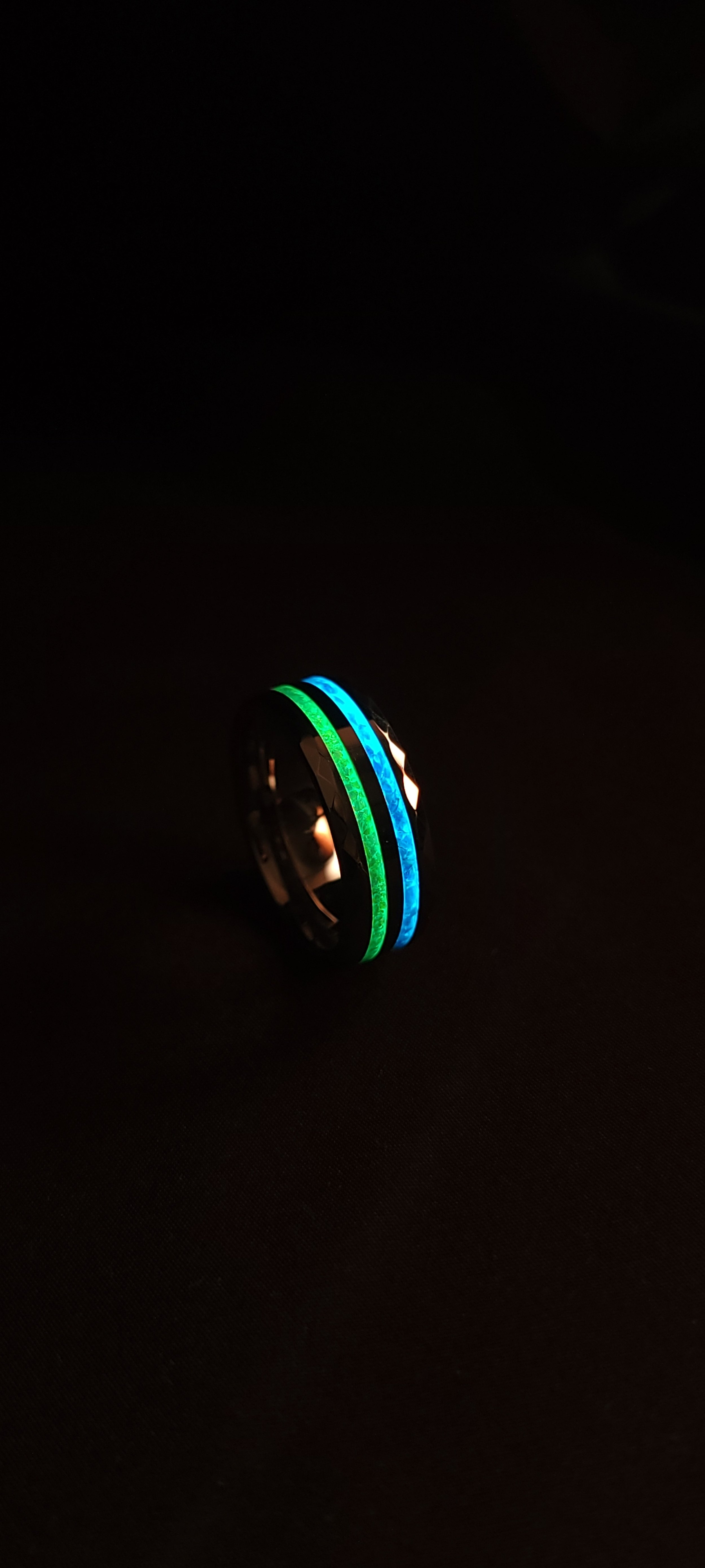 A faceted, double channel, tungsten band made with light green and blue opal. Each channel glows its corresponding colors. 
