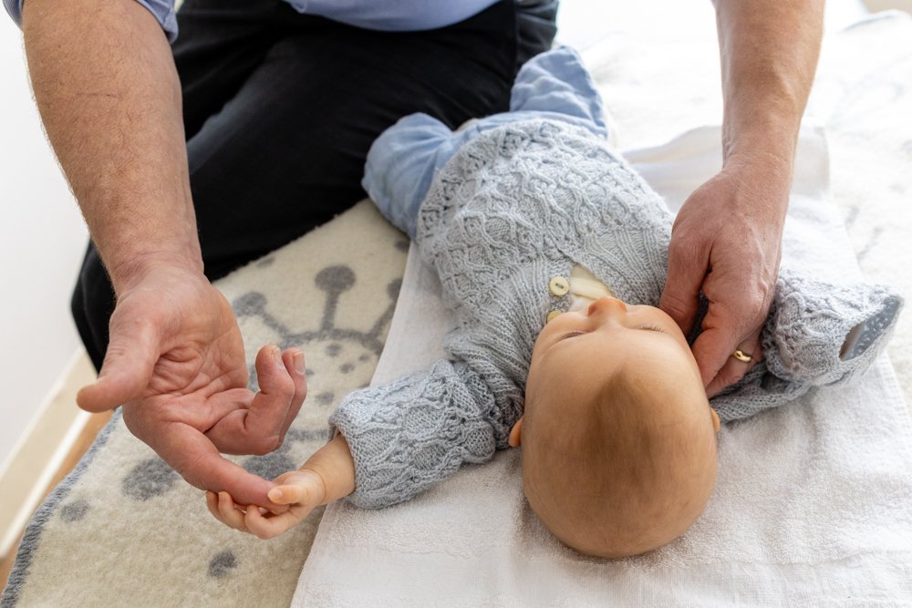 Infant holding a chiropractor's finger during pediatric chiropractic care