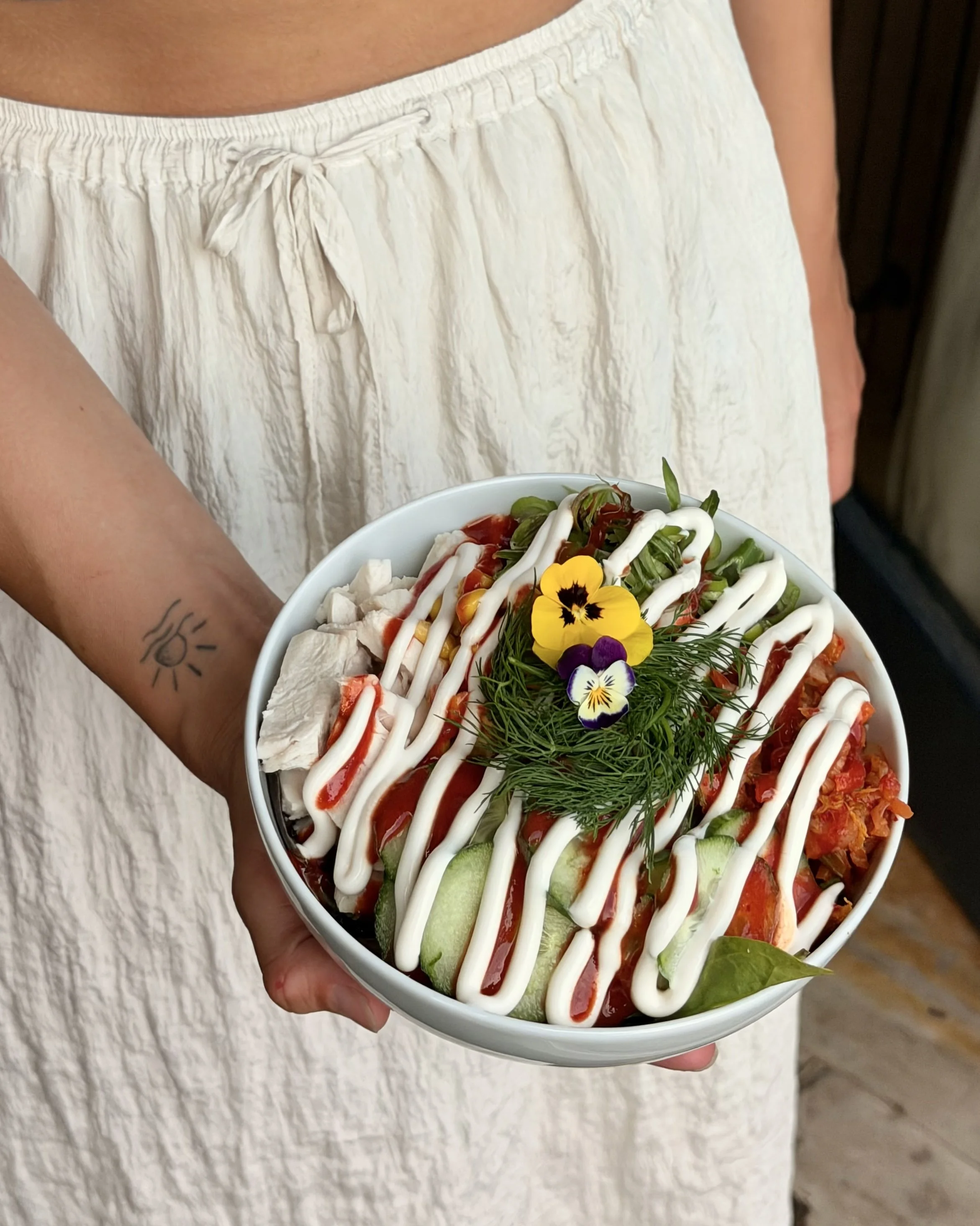 Person holding a bowl of salad with vegetables, garnished with edible flowers and drizzled with dressing.