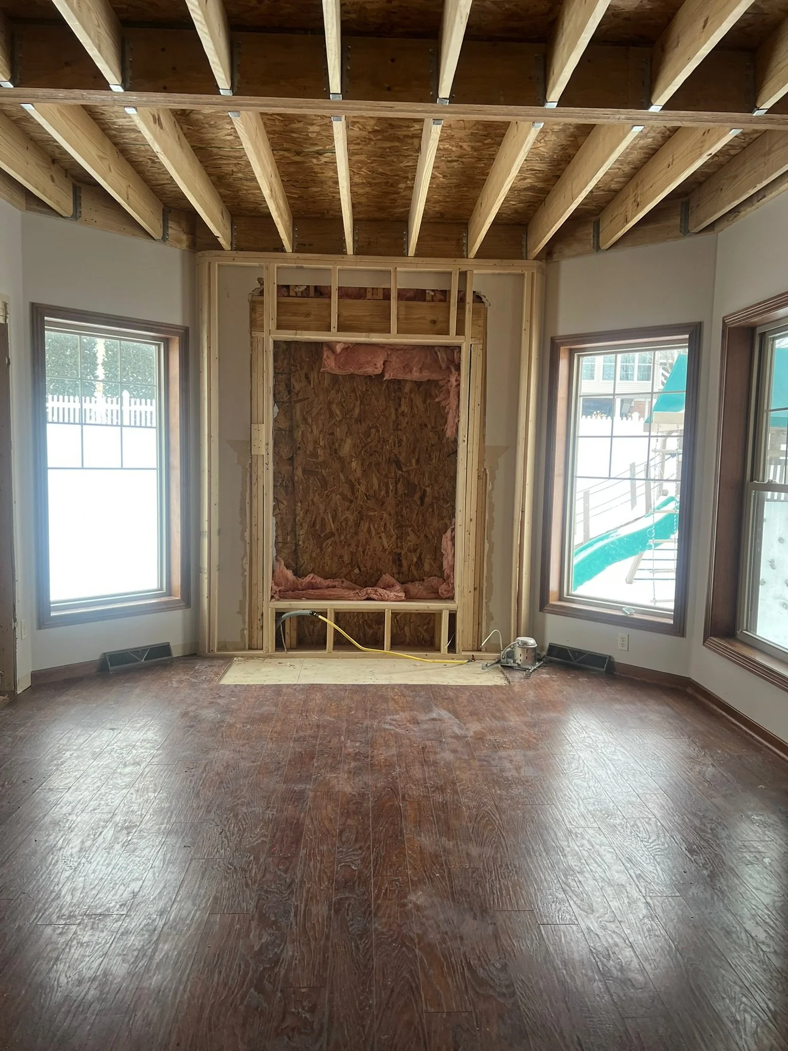 Room under construction with wooden framing around a window, open space in the wall, insulation, and construction tools on the floor.