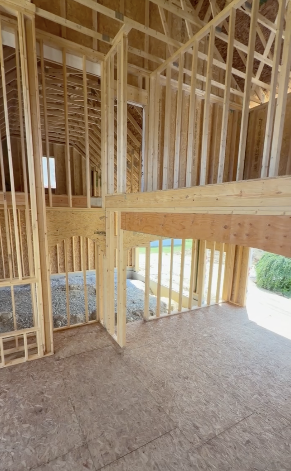 Wood framing for a house under construction with visible studs and beams, unfinished interior, and a partly open wall with views of the outdoors.