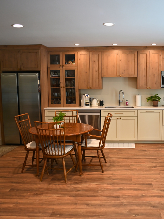Kitchen with wooden cabinets, stainless steel refrigerator, small wooden dining table with four chairs, and various kitchen appliances.