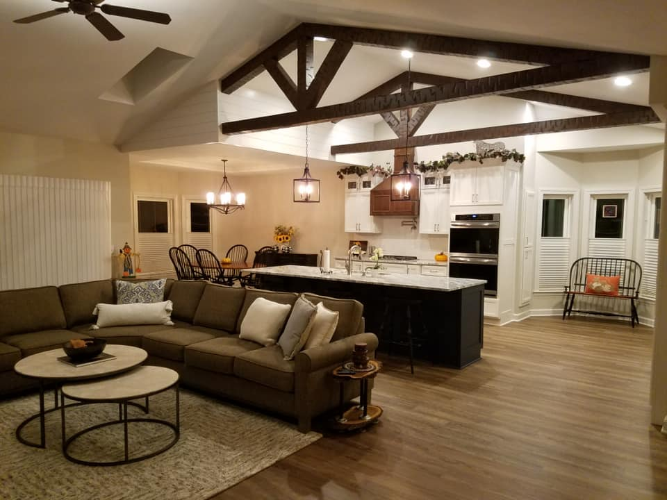 Open-concept living room and kitchen with wooden beams, modern furniture, and cozy lighting.