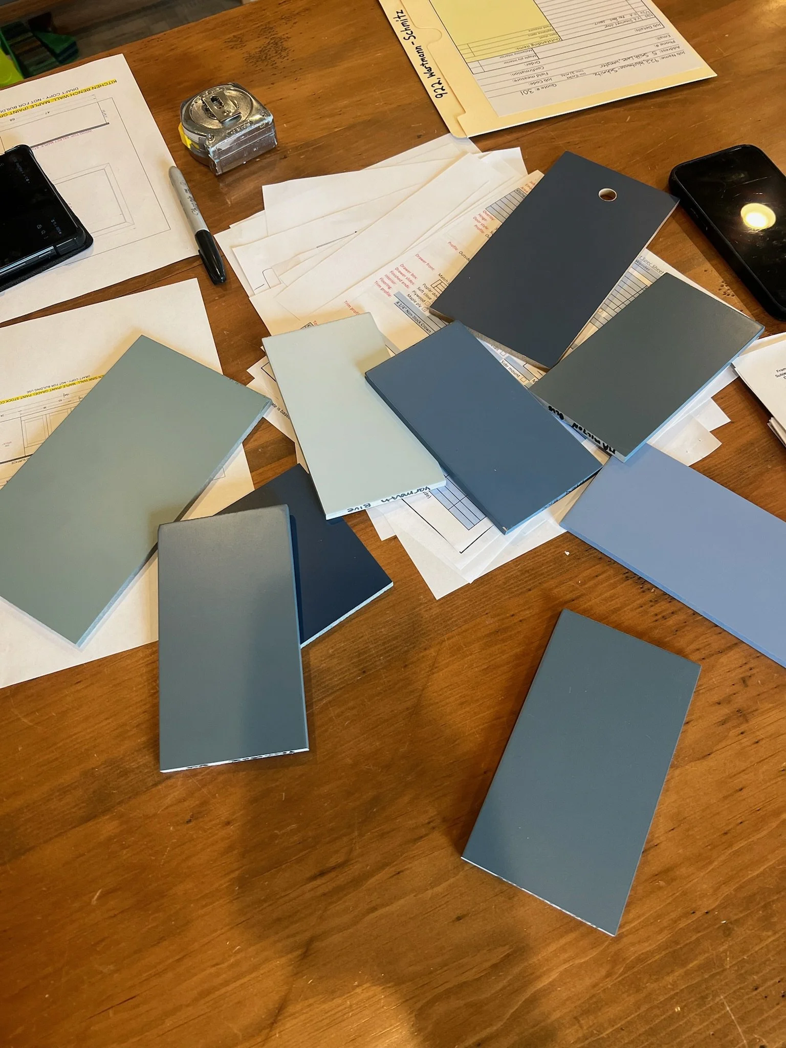 Various paint swatches, papers, a tape measure, a pen, and two smartphones on a wooden table.