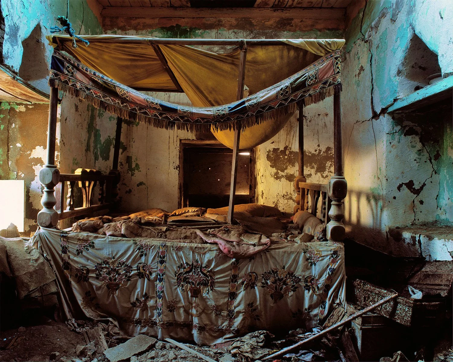 An abandoned, dusty bedroom with a broken canopy bed and torn fabric.