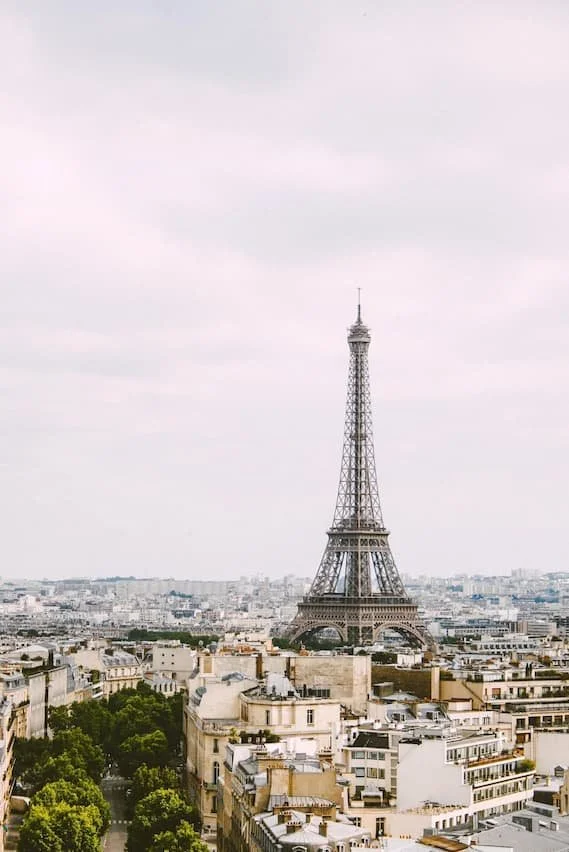 Eiffel Tower in Paris, France, seen from a distance over city buildings with cloudy sky.