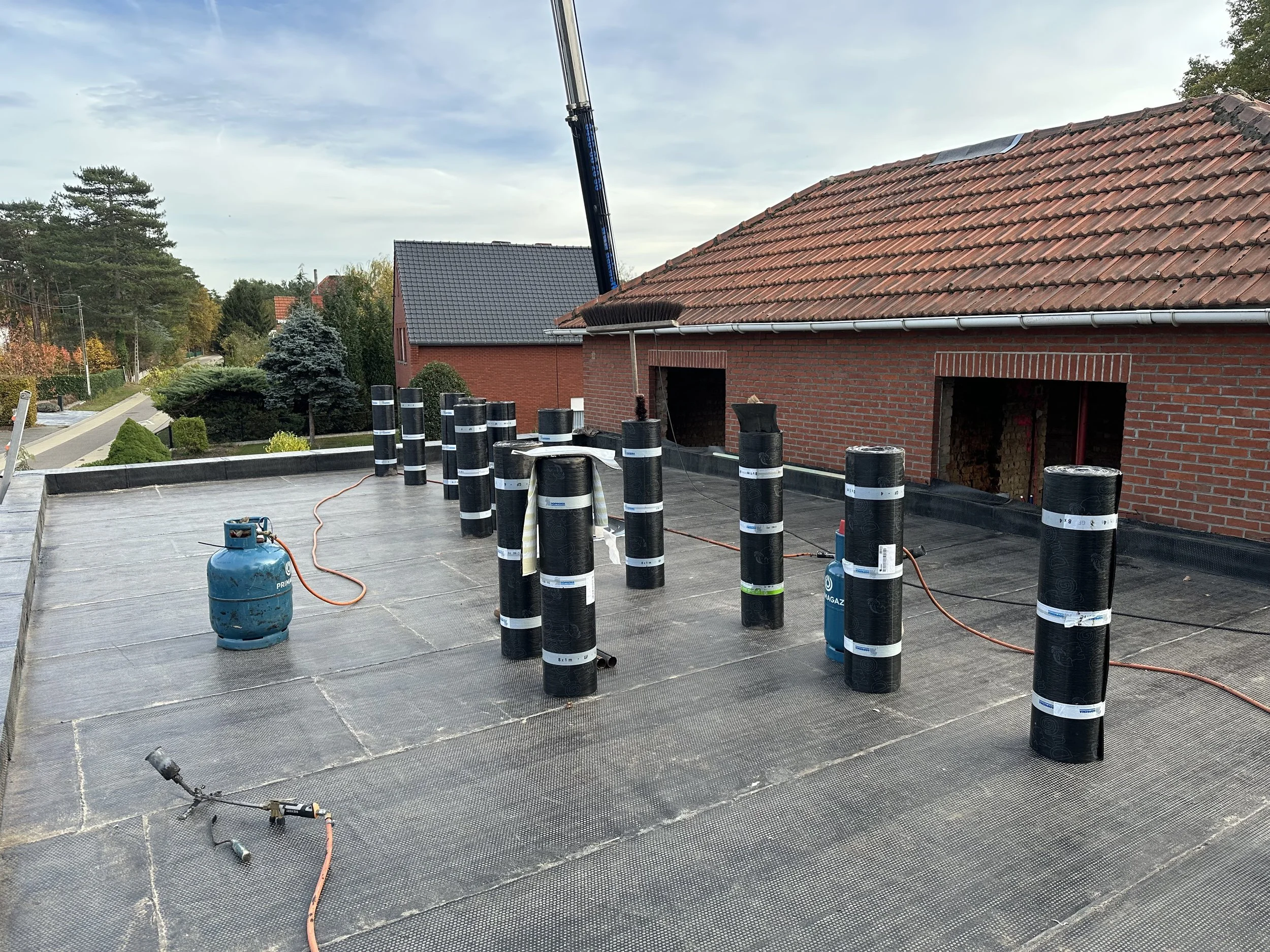 Op een plat dak in Geel wordt waterdichting aangebracht met isolatieplaten en een laag bitumen.
