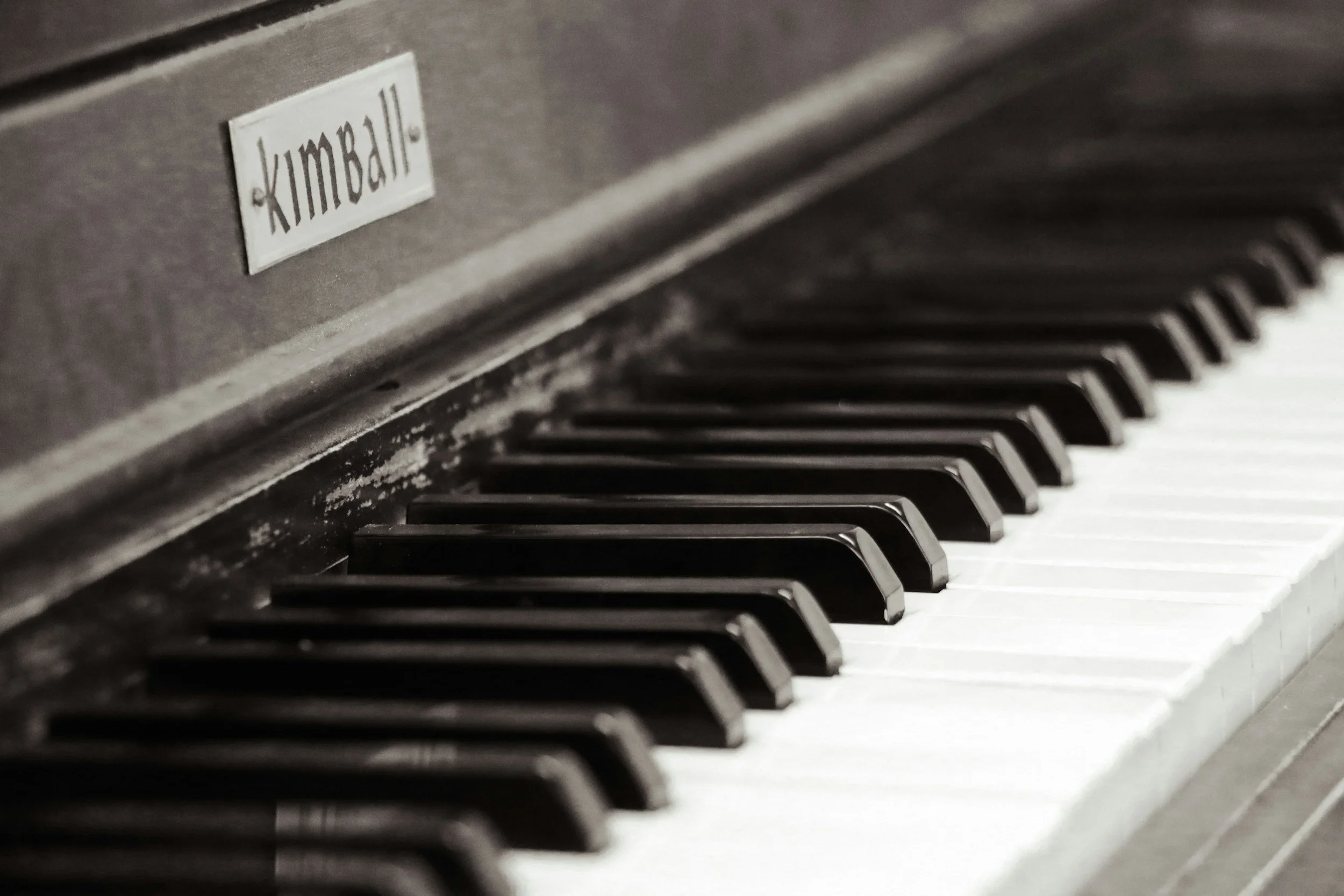 Close-up of a piano keyboard showing black and white keys with a metal sticker labeled 'kimball' on the piano body above the keys.