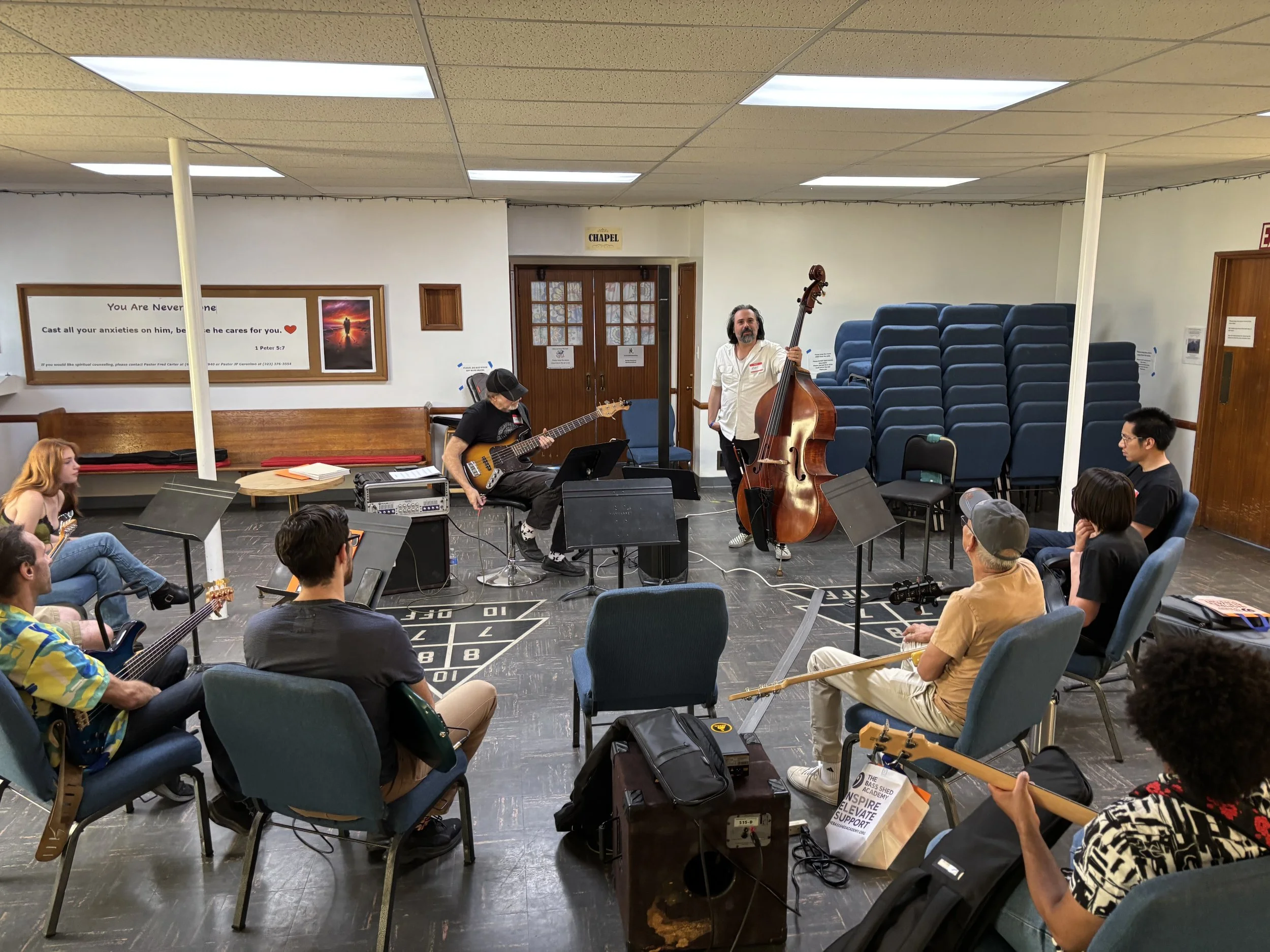 People playing musical instruments and an audience seated in a room with a sign that reads 'Chapel' above a door.