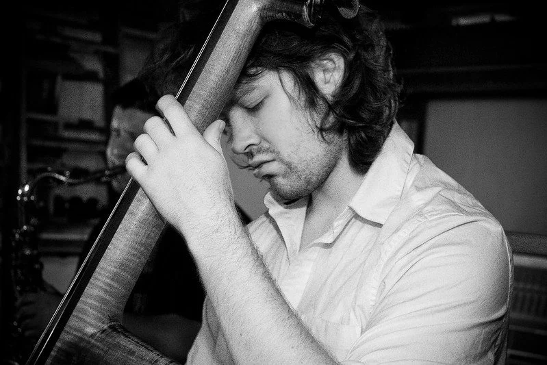 Black and white photo of a man playing a double bass with eyes closed, focusing intently.