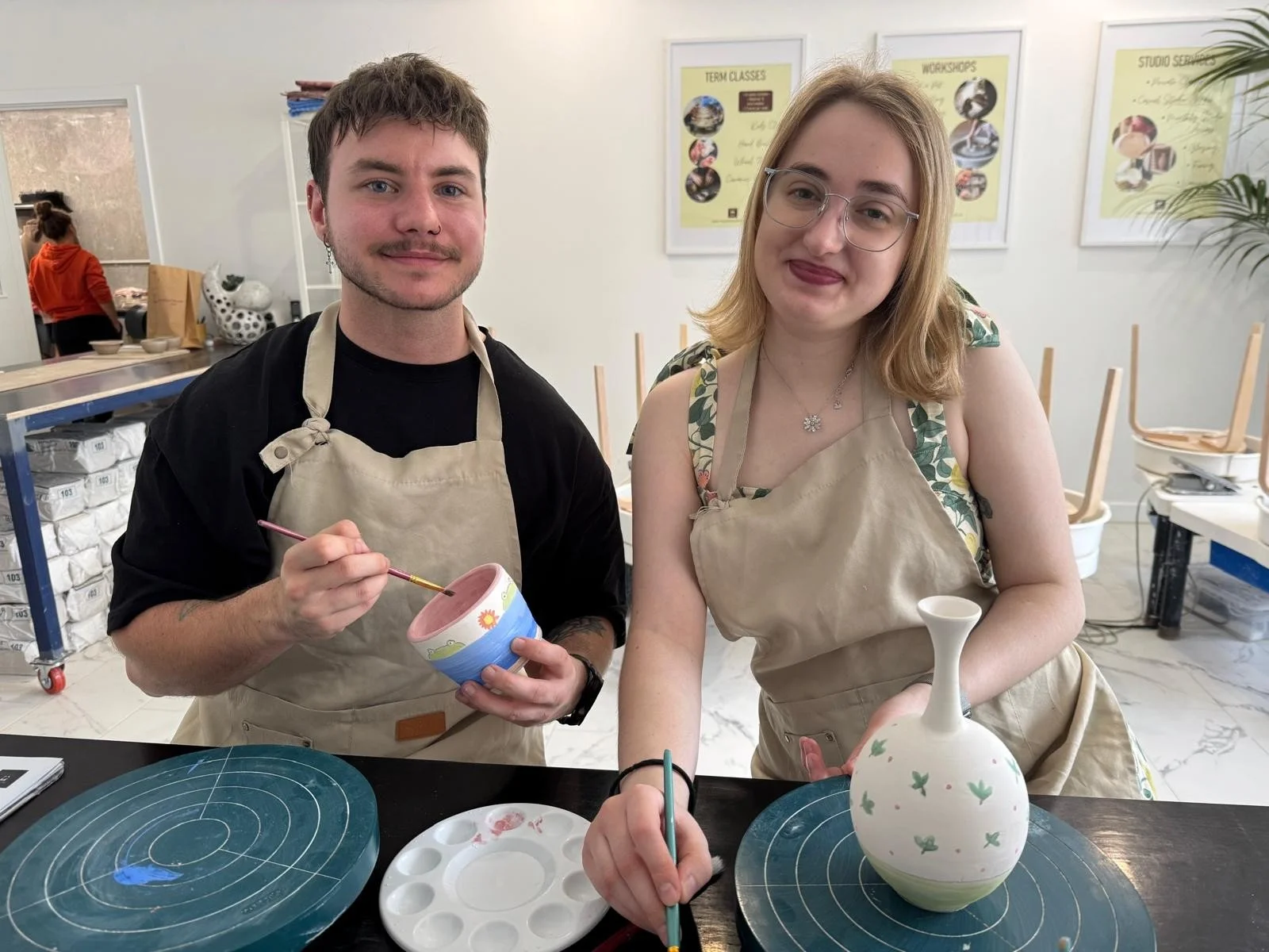 Two people enjoying a creative session at the Paint and Sculpt Cafe at Kingston Clay Studio in Braeside, painting handmade ceramic pottery pieces.