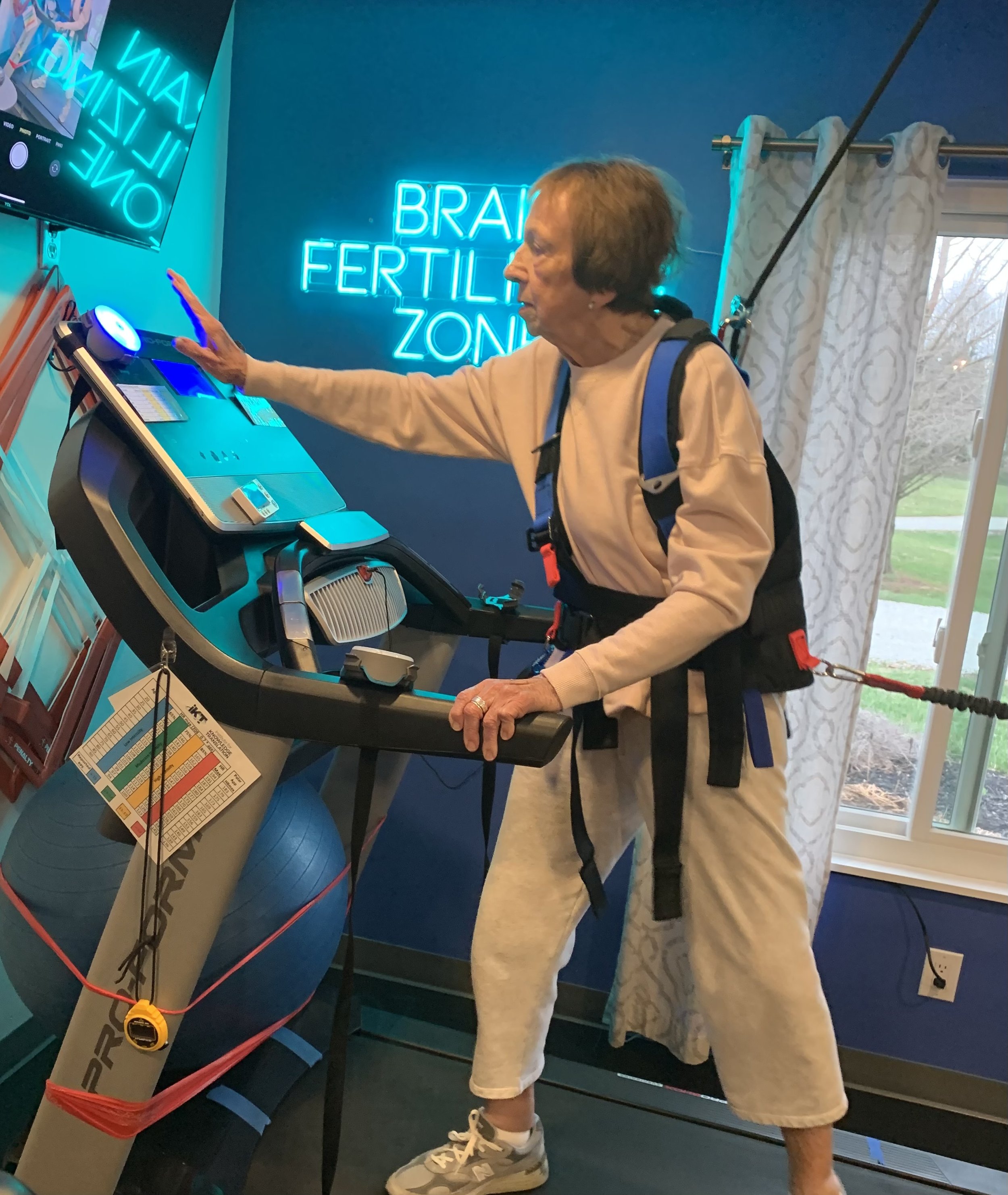 Woman wearing a safety harness while walking on treadmill with resistance and practicing dual task training at Empower Balance in Waynesville.