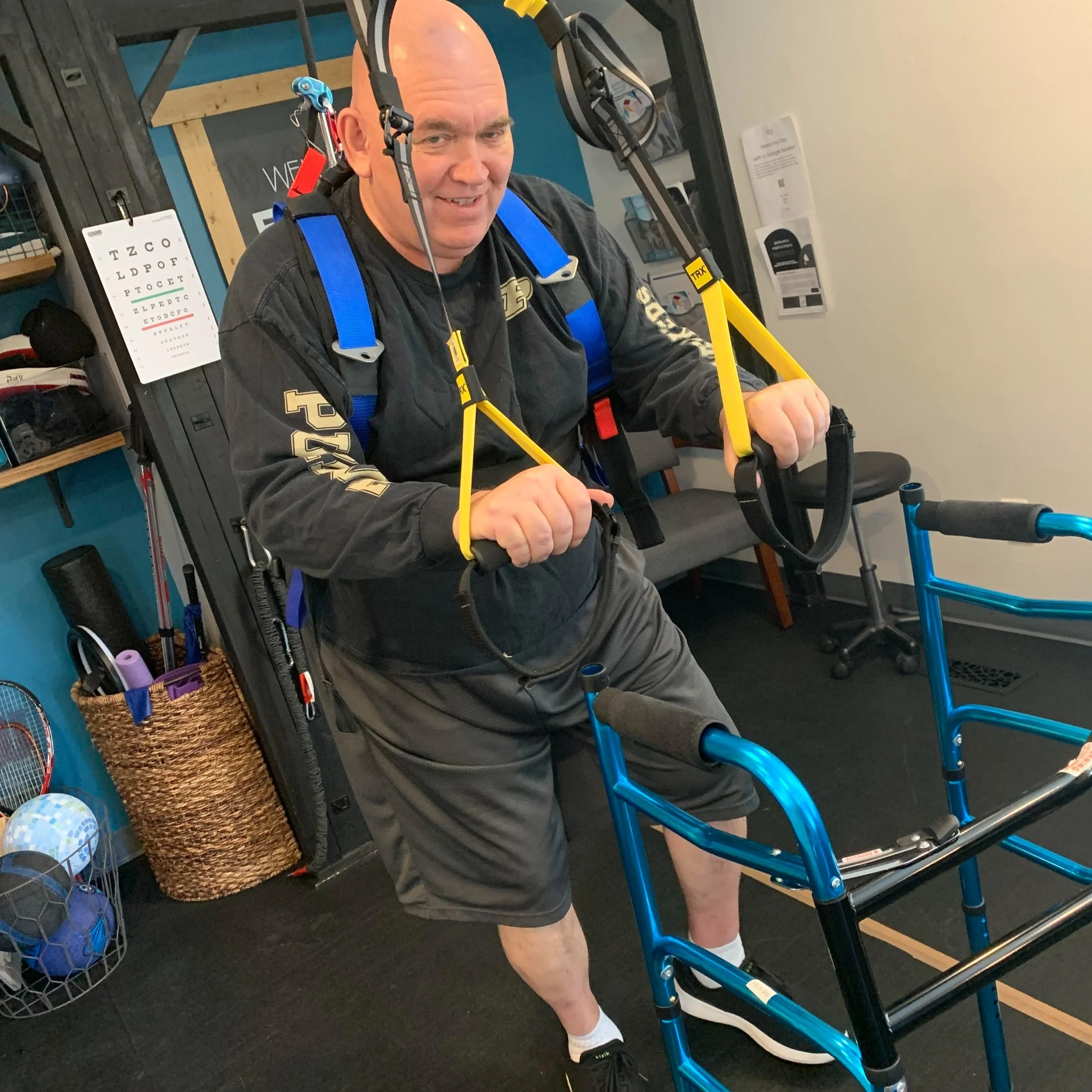 Smiling man with walker and balance harness exercising at Empower Balance with colorful background.