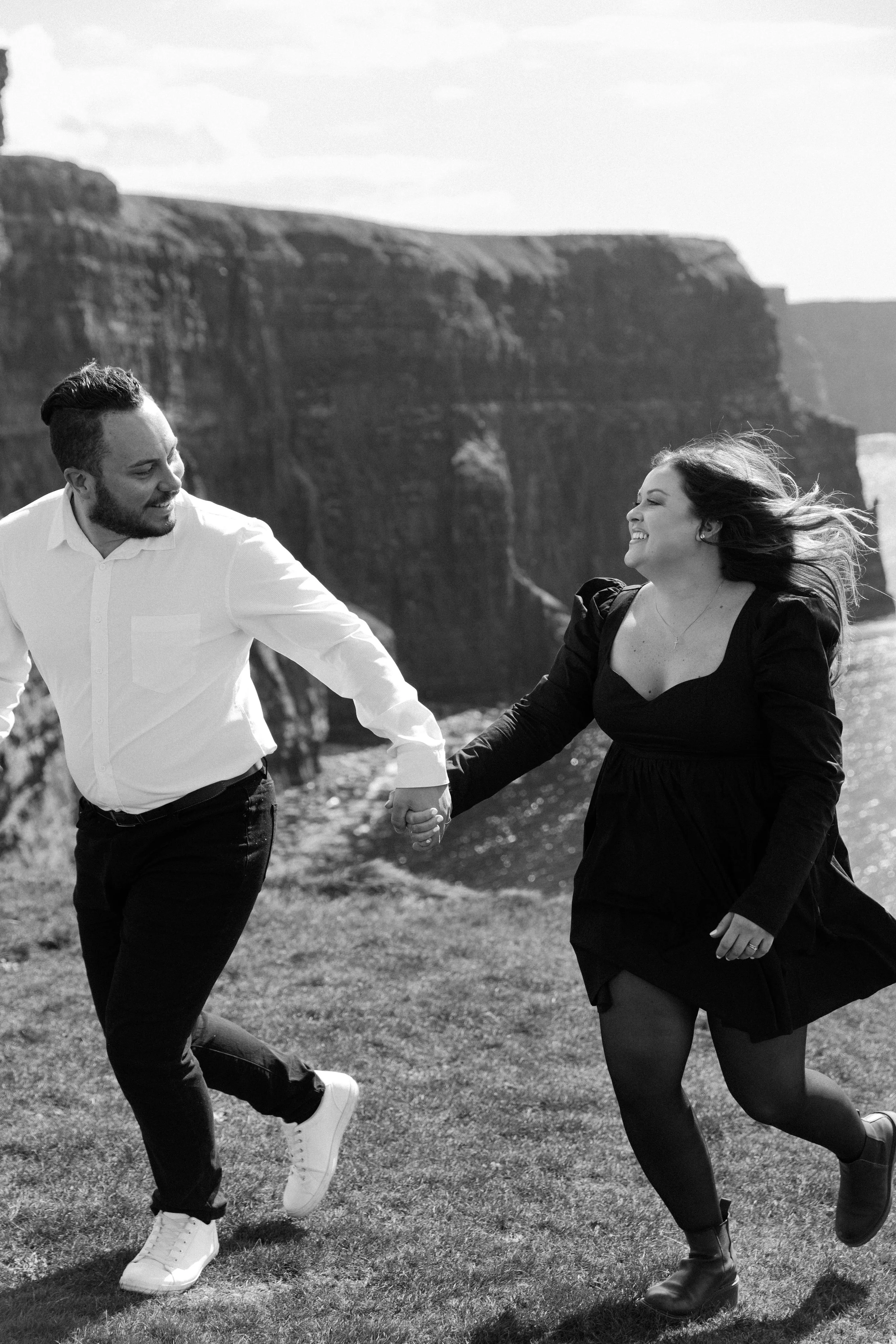 Couple holding hands running cliffs of mower Ireland engagement