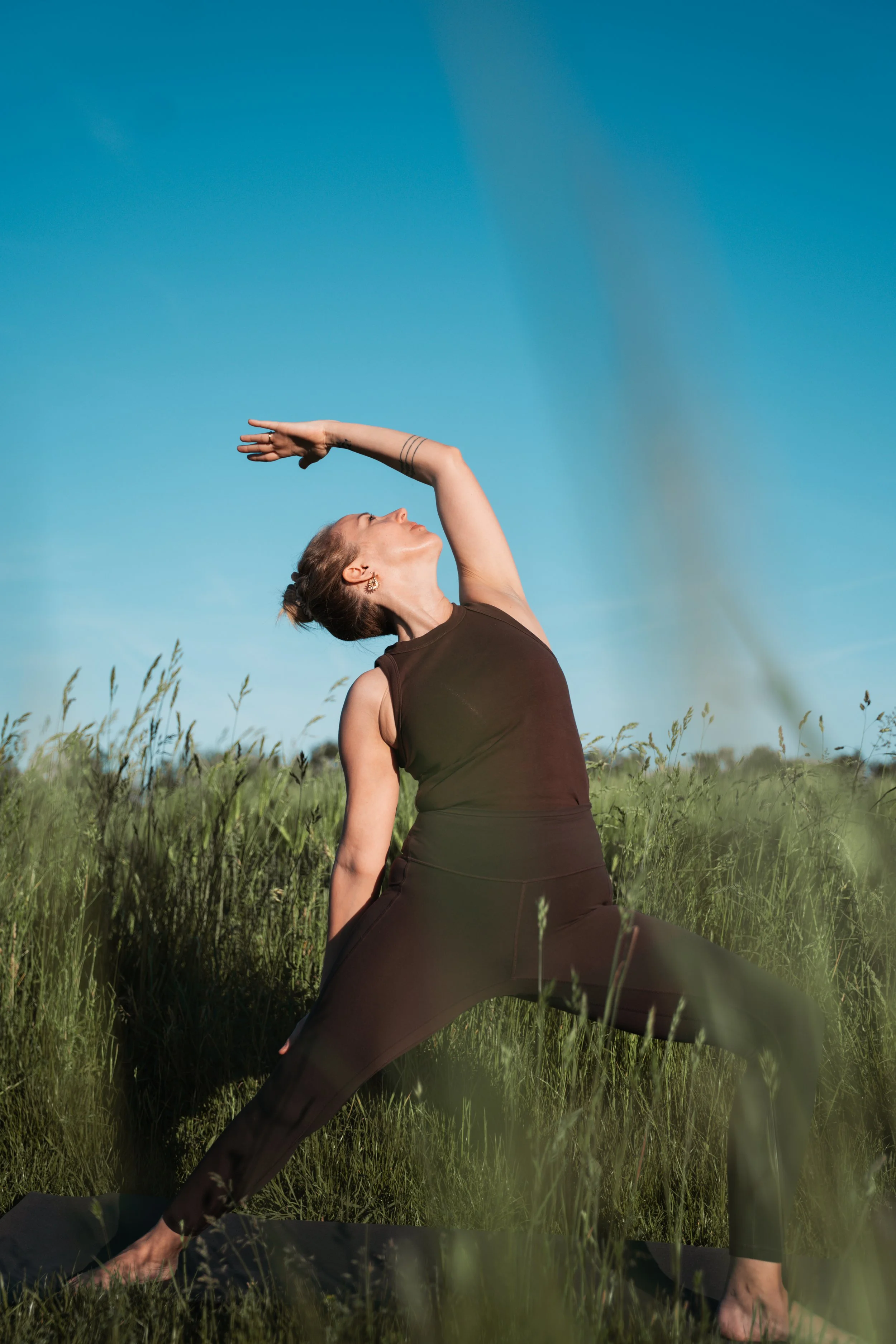 Frau macht Yoga im Freien auf einer Wiese unter blauem Himmel.