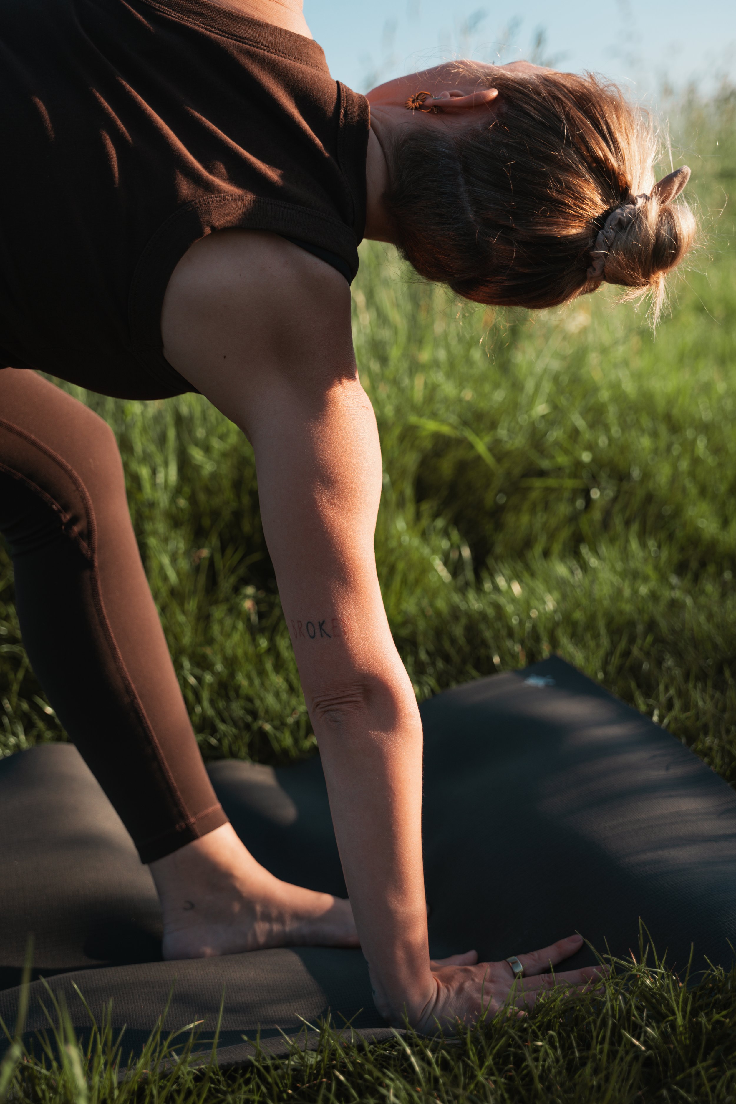 Eine Person macht eine Yoga-Pose im Freien auf einer Matte, umgeben von Gräsern bei Sonnenuntergang.