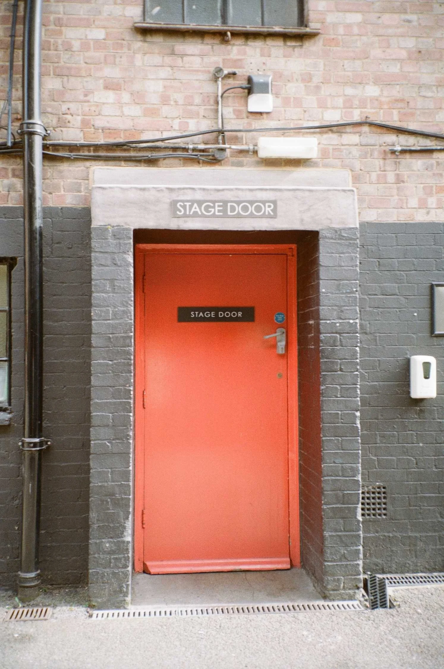 A red door outside with a black sign on it saying stage door.