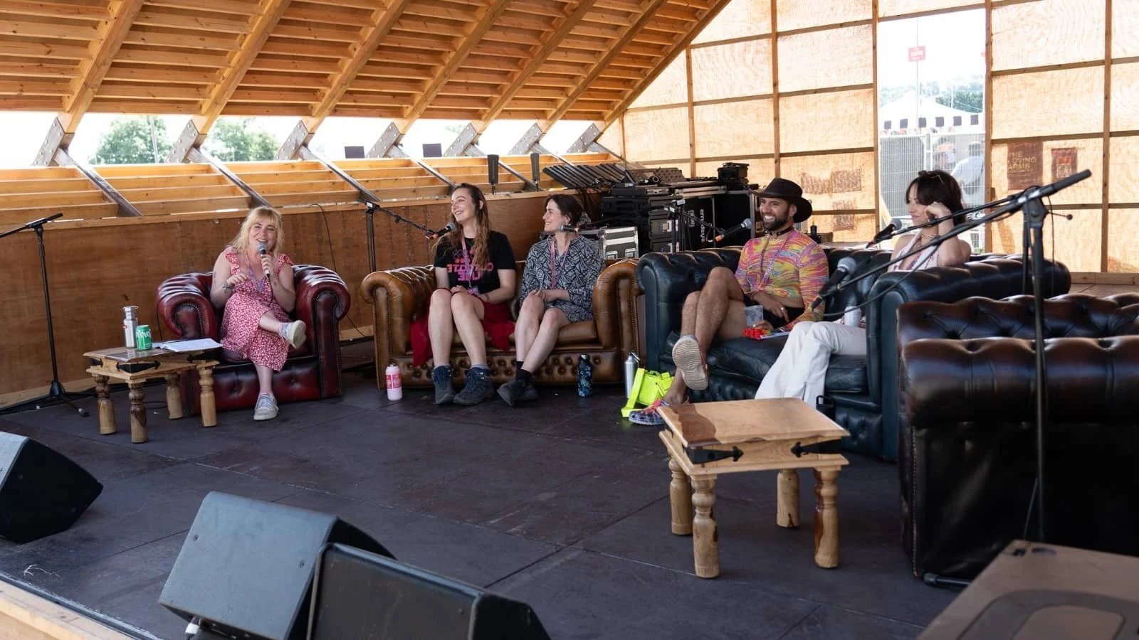 Five people on stage at an outdoor festival sitting on leather couches with microphones for a panel discussion.